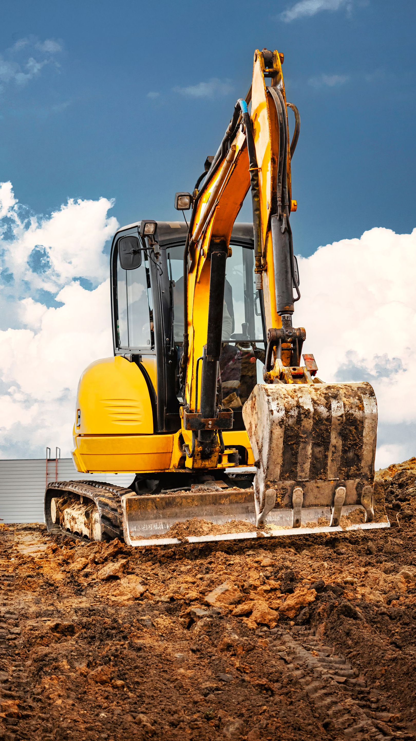 Une pelleteuse jaune creuse dans de la terre brune, sur fond de ciel bleu.