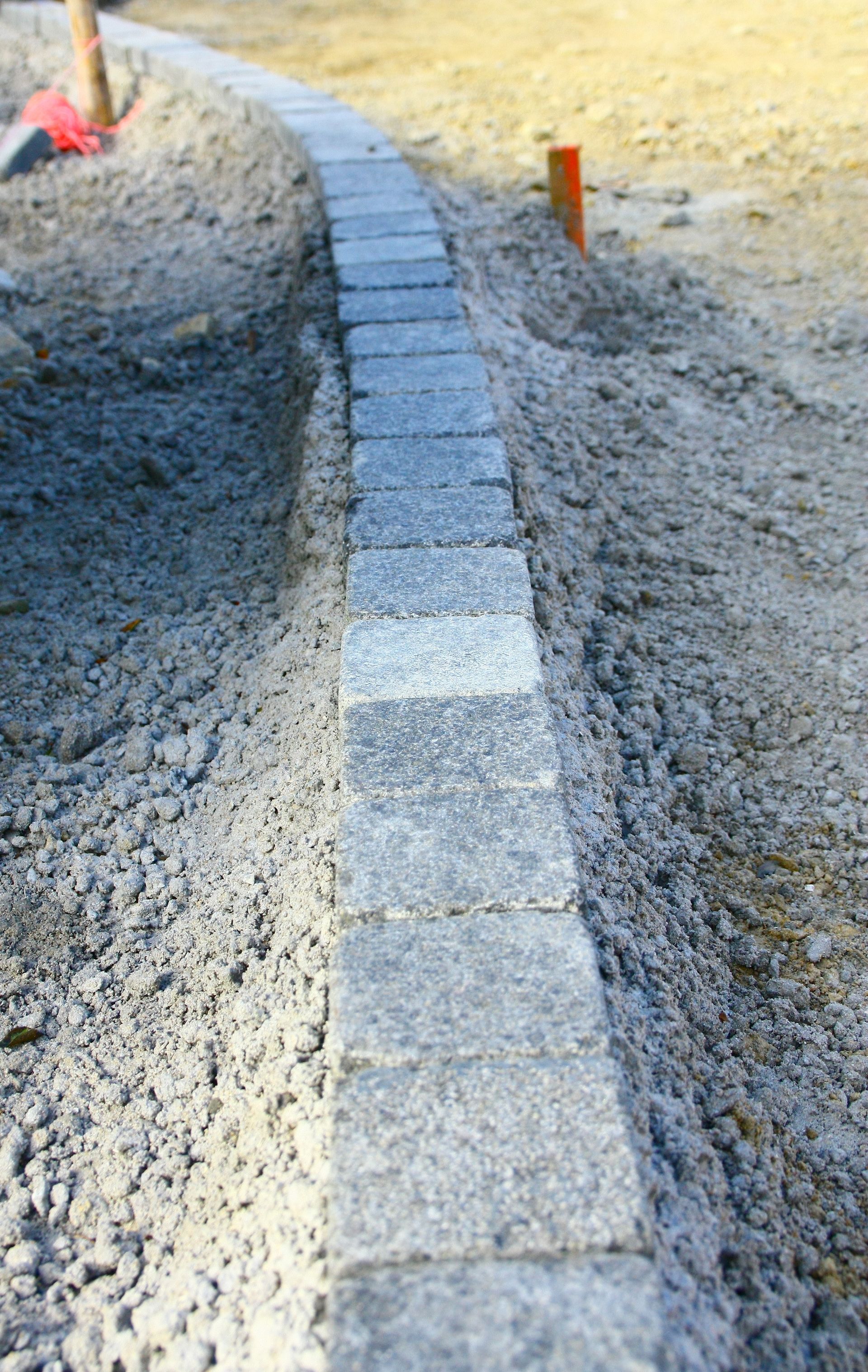 Des dalles de pierre bordent une allée courbe, posées sur du gravier et de la terre.