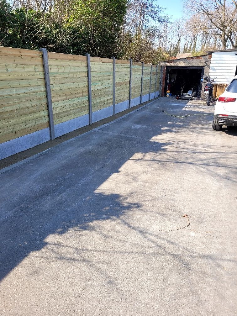 Longue allée bordée d'une clôture en bois à gauche et d'un garage en arrière-plan. Voiture garée à droite.