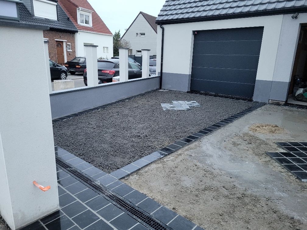 Allée de gravier bordée de pierres, avec un garage et une maison visibles en arrière-plan.