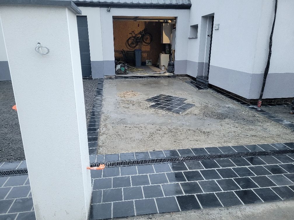 Allée en construction avec bordure en briques noires, menant à un garage.