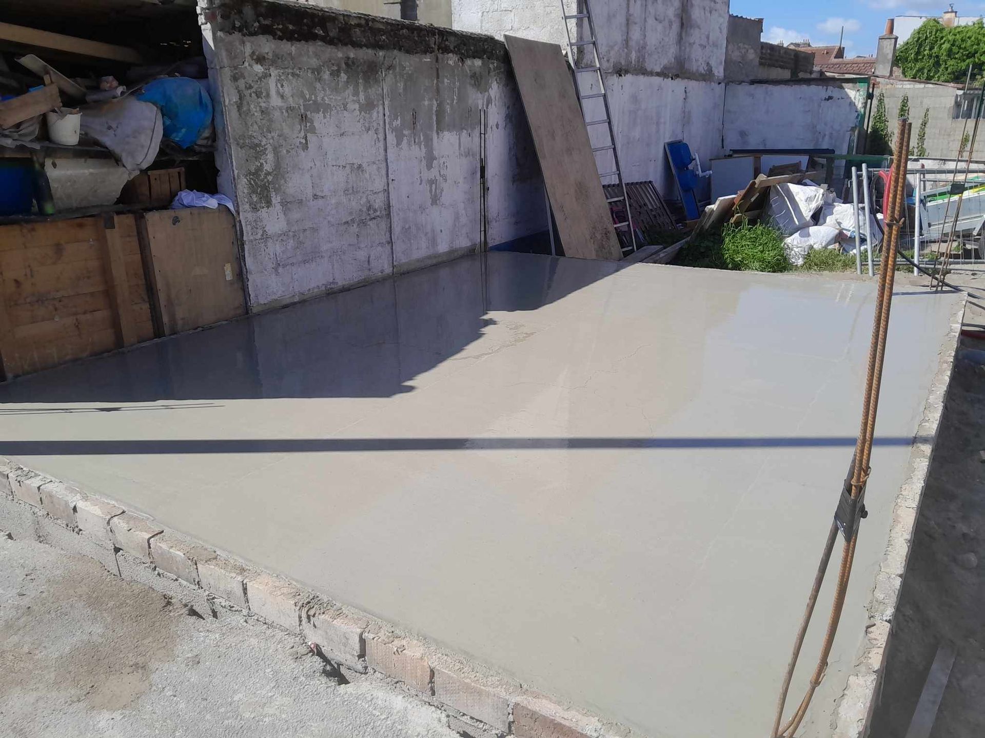 Terrasse en béton fraîchement coulé, de couleur grise, contre un mur blanc et gris.