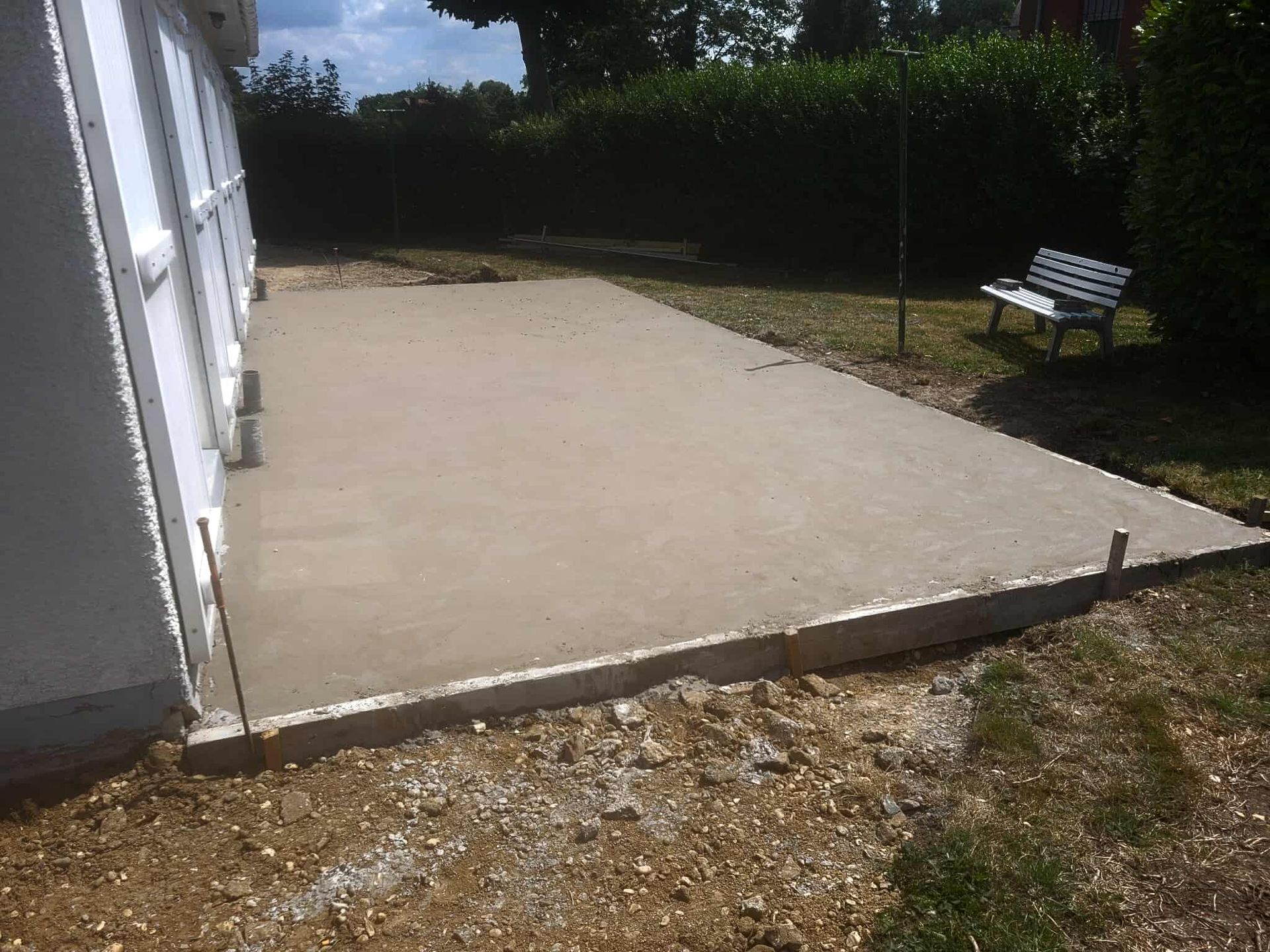 Terrasse en béton fraîchement coulée à côté d'une maison blanche, sur un terrain gazonné.