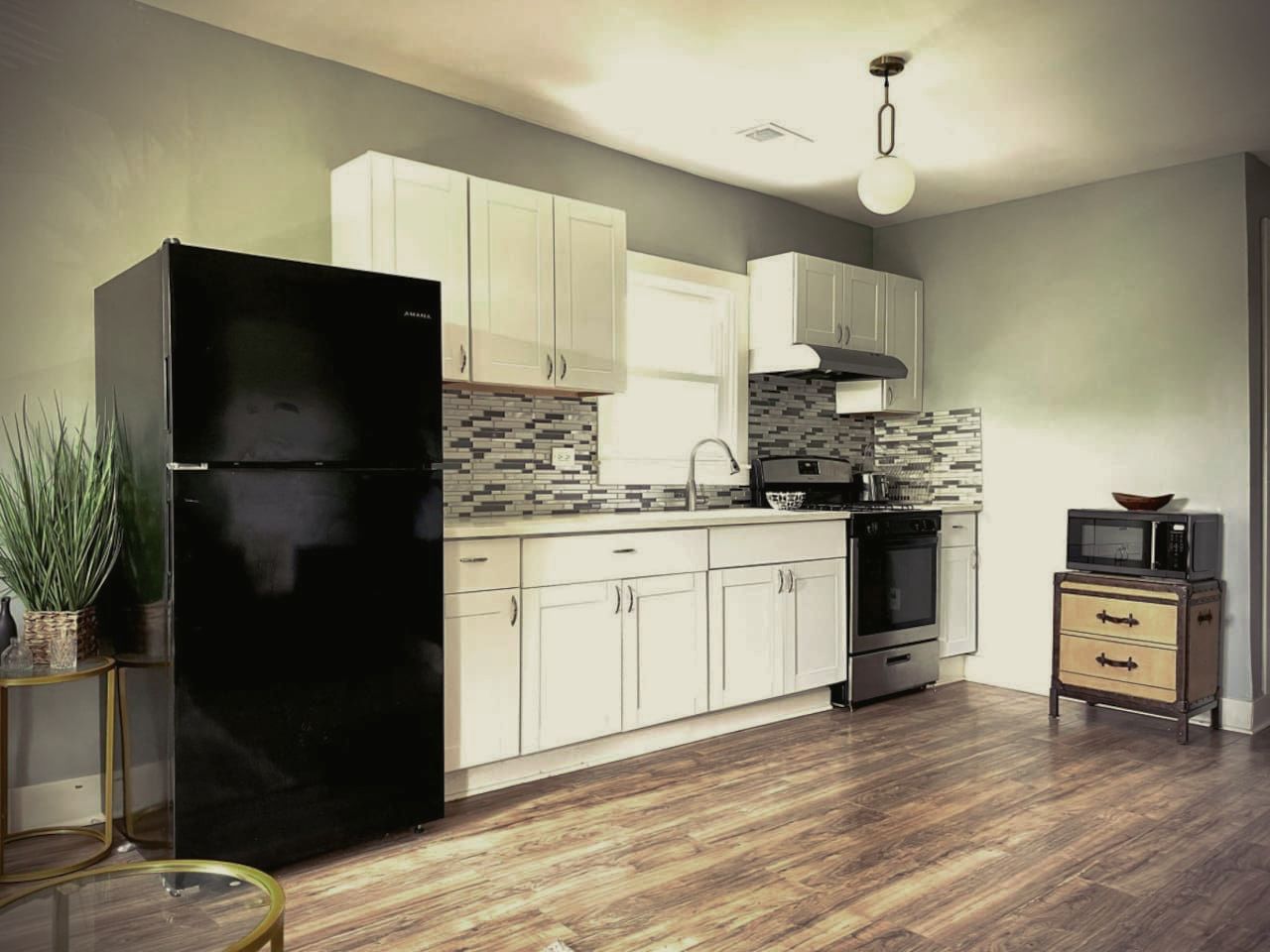 A kitchen with white cabinets , a black refrigerator , a stove , and a microwave.
