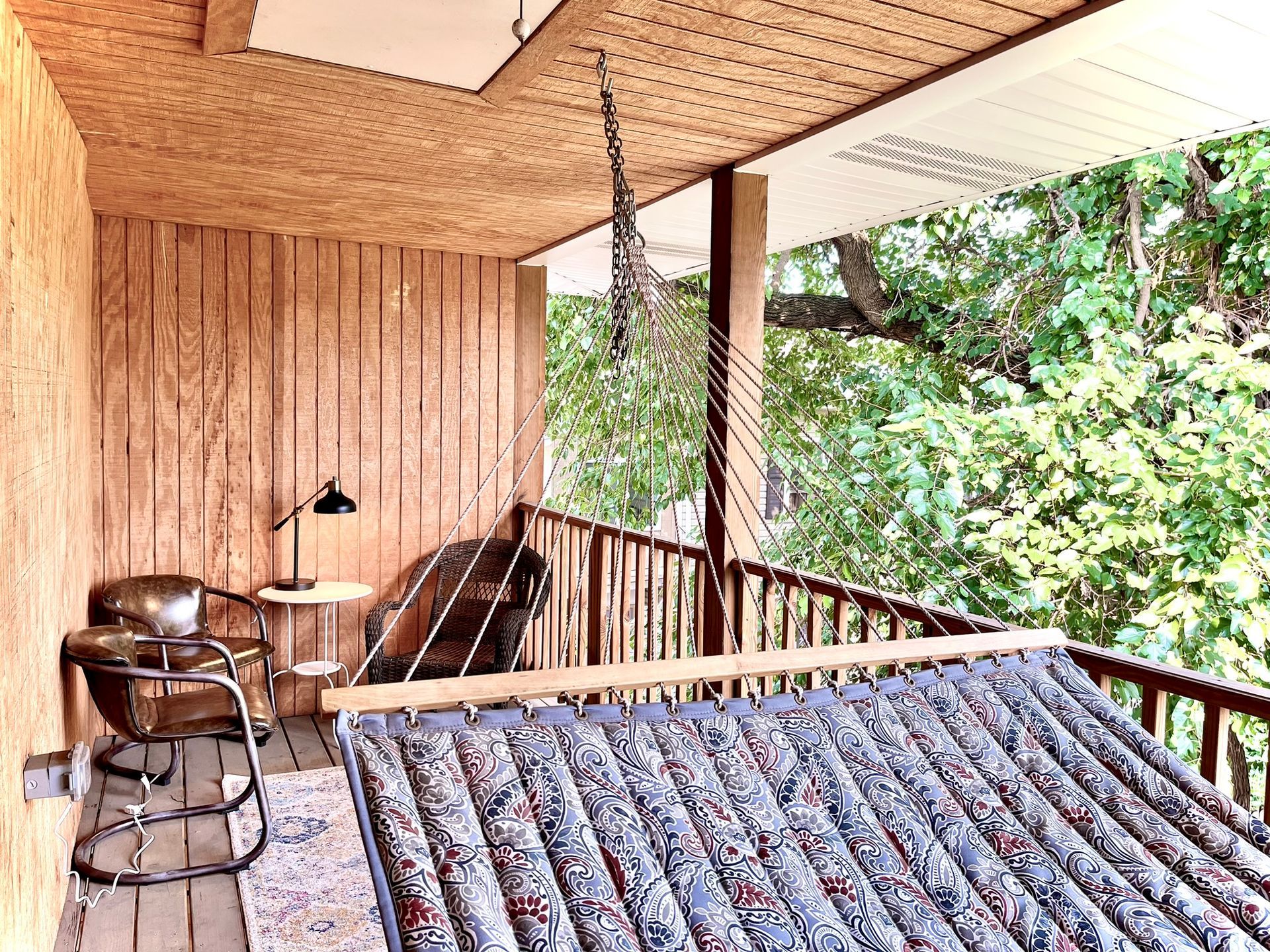 A porch with a rocking chair and a hammock hanging from the ceiling.