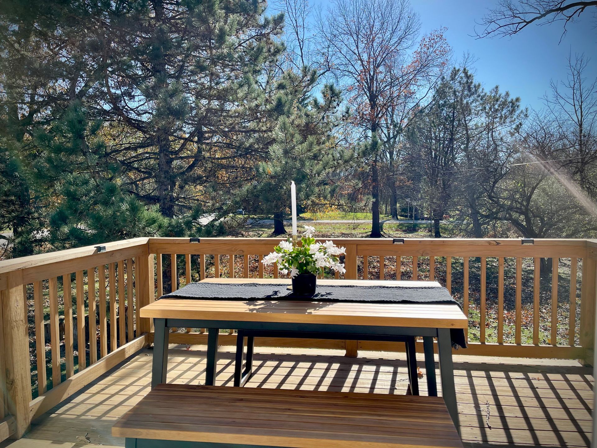 A wooden table and bench on a deck with trees in the background.