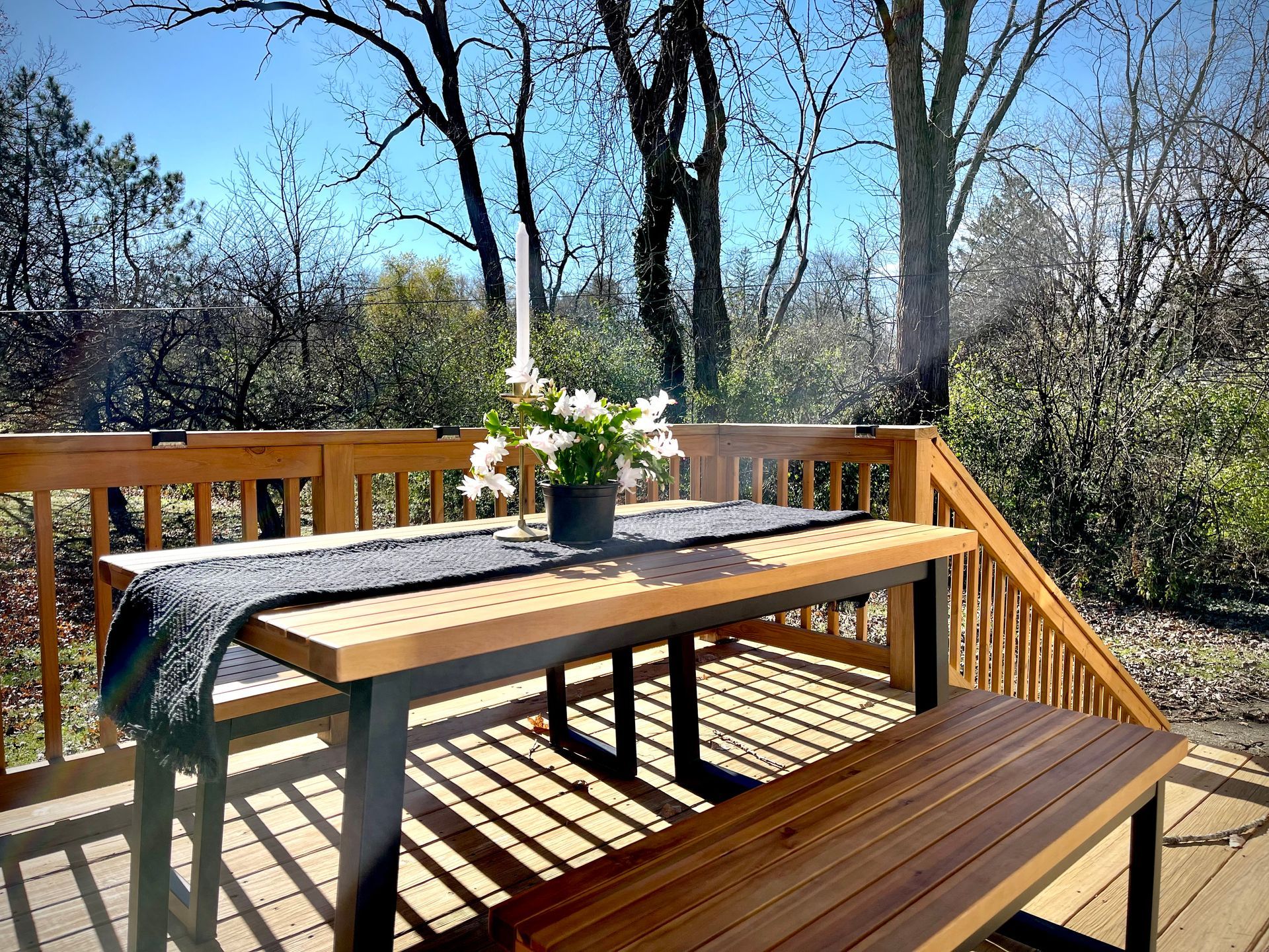 A wooden table and bench on a deck with trees in the background.