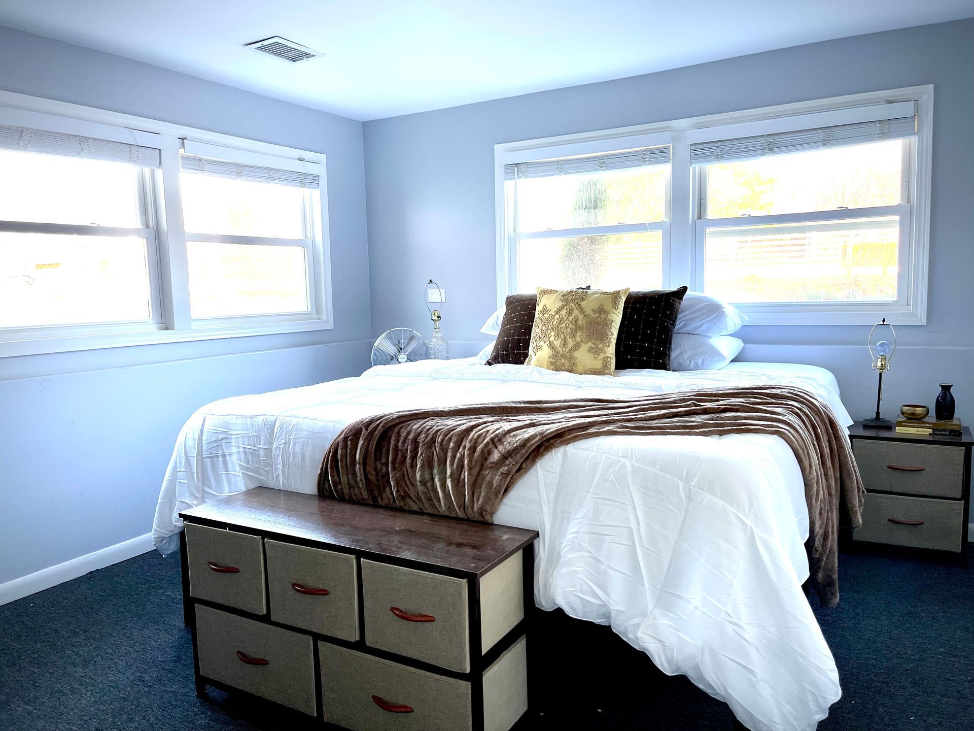 A bedroom with a bed , dresser , nightstand , and two windows.