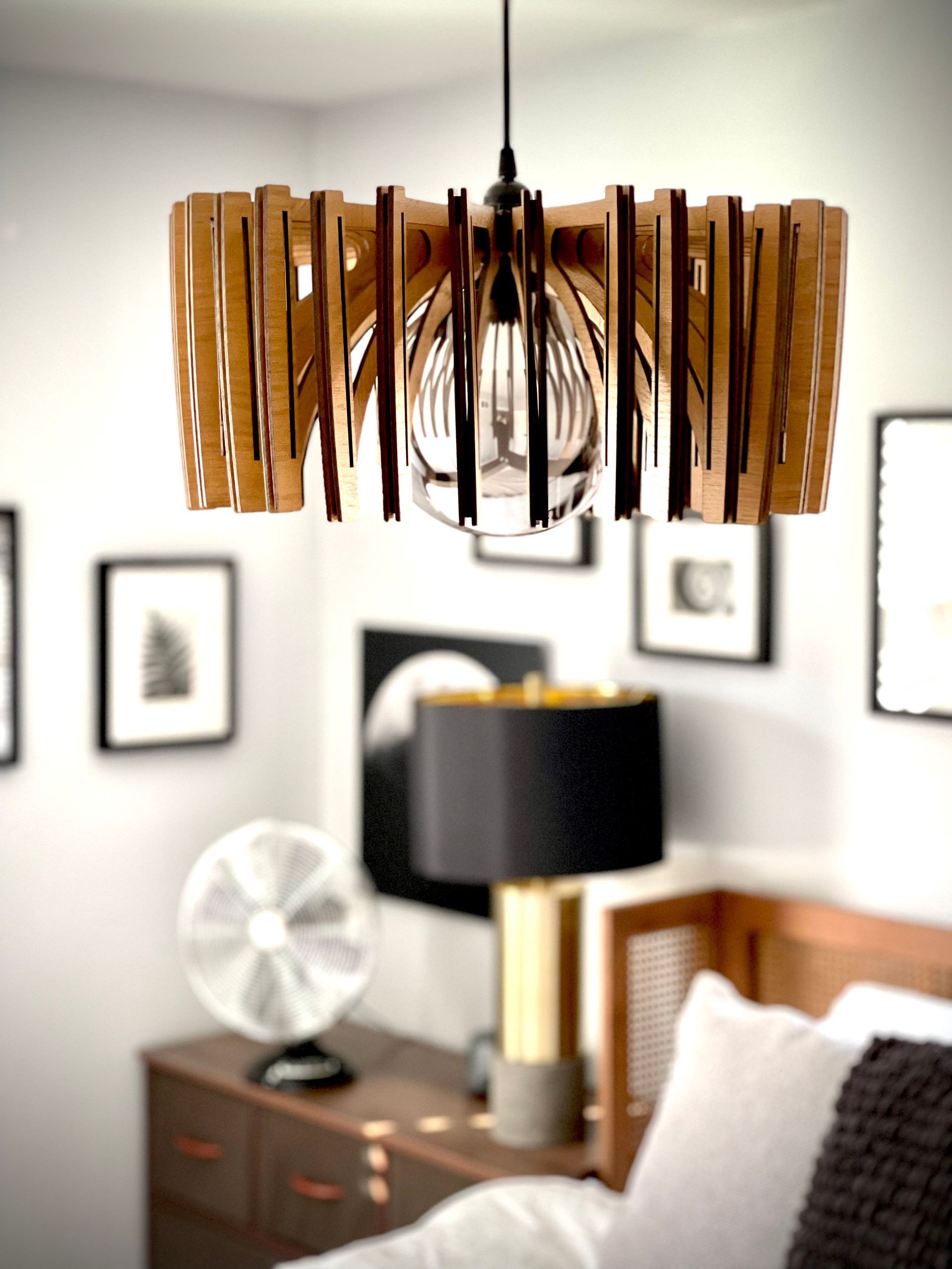 A bedroom with a bed , dresser , lamp and a pendant light hanging from the ceiling.