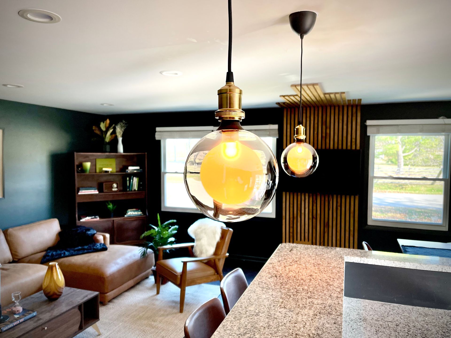 A living room with a couch , chairs , and a pendant light hanging from the ceiling.