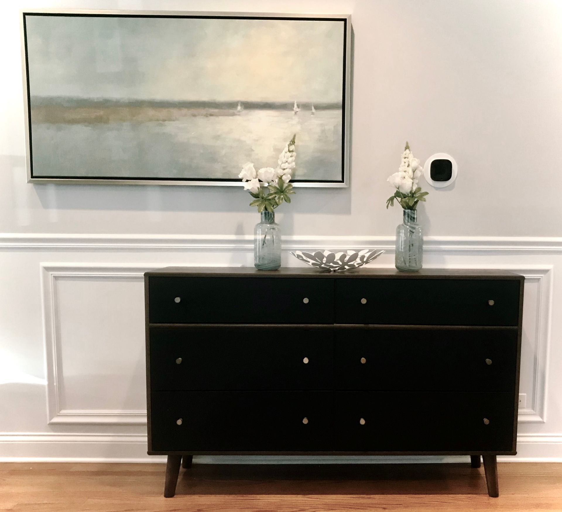 A black dresser with two vases of flowers and a painting on the wall above it