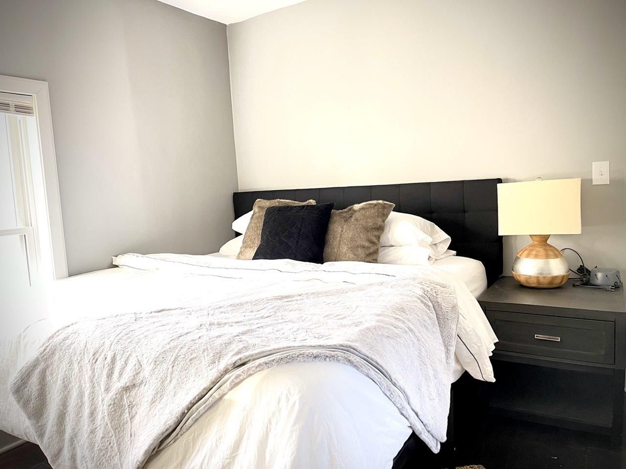 A bedroom with a bed , nightstand , lamp and mirror.