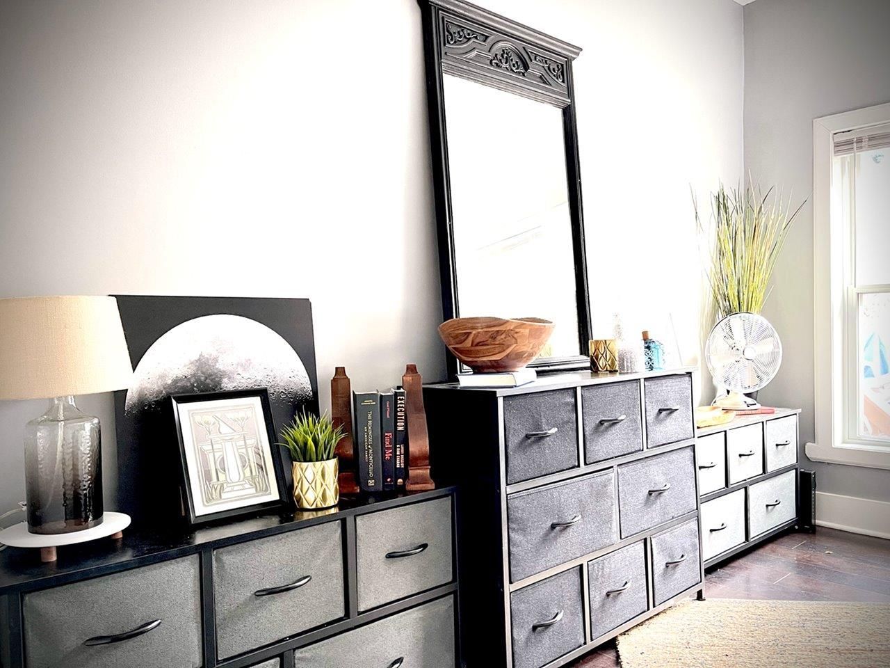 A bedroom with a dresser , mirror , and lamp.