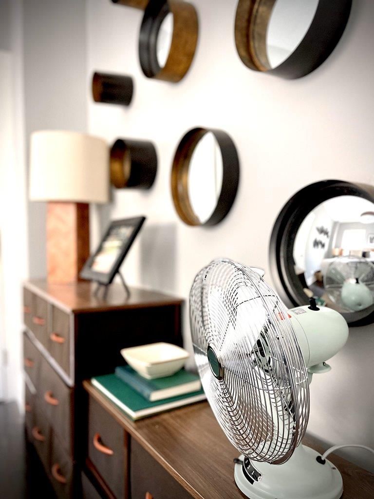 A fan sits on a dresser in a room with mirrors on the wall