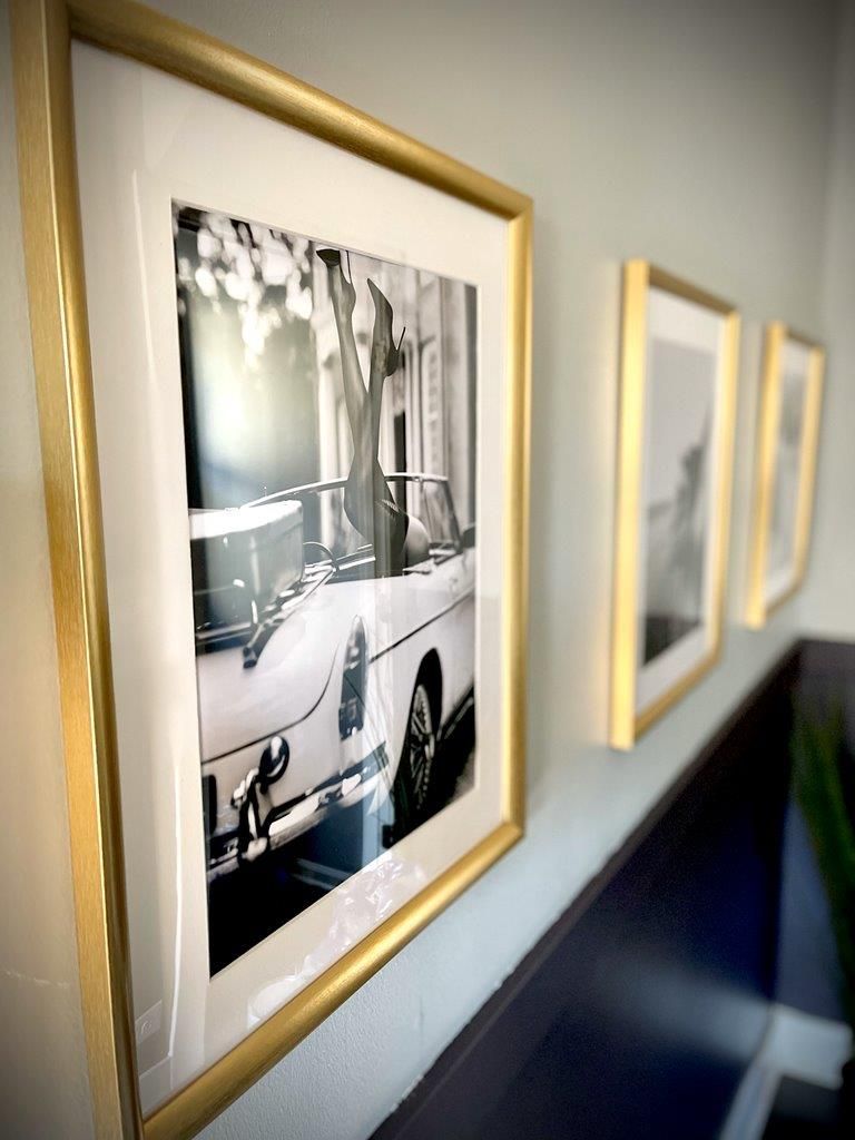 A black and white photo of a car is framed on a wall.