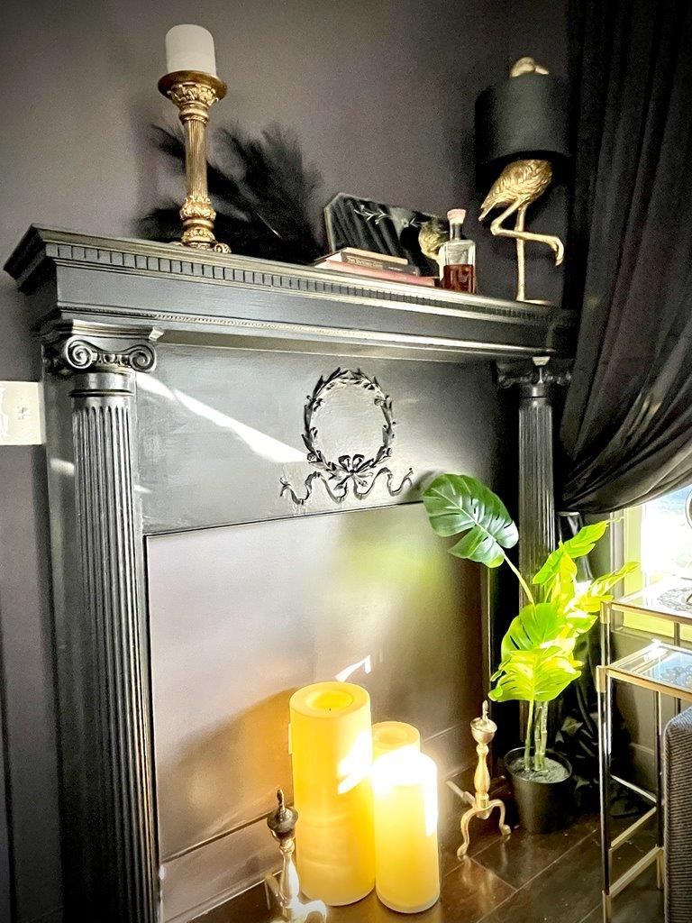 A black mantle with candles and a lamp on top of it.