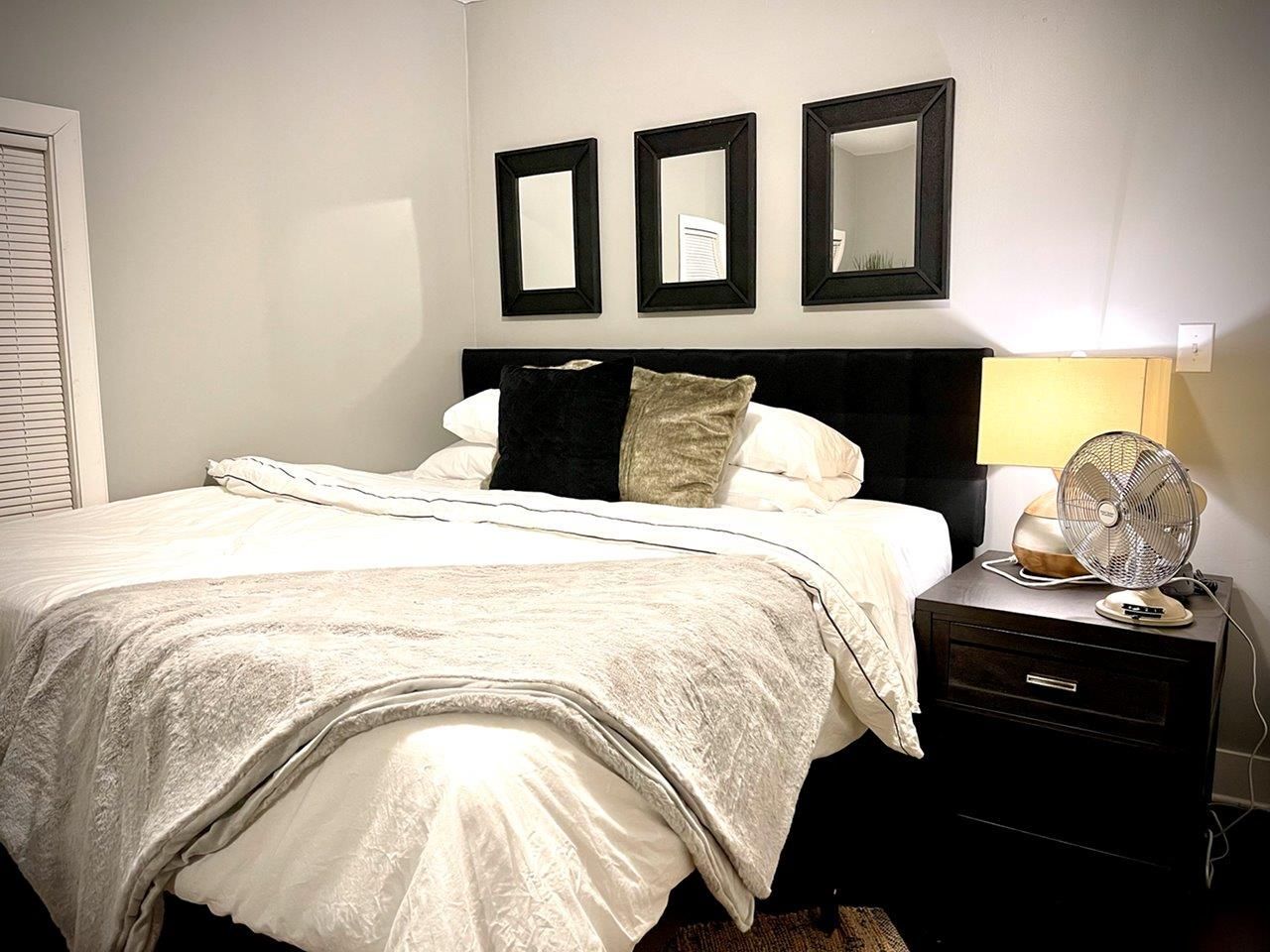 A bedroom with a bed , nightstand , lamp and mirrors on the wall.