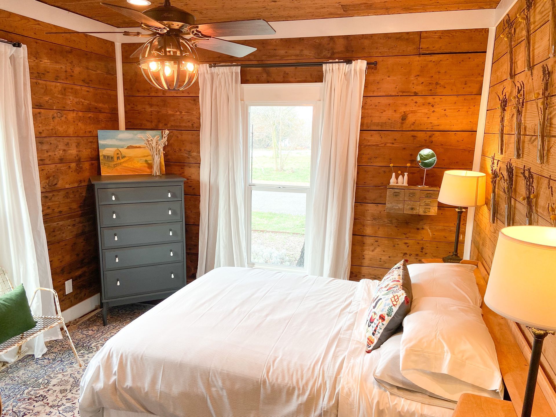 A bedroom with a bed , dresser , lamps and a ceiling fan.