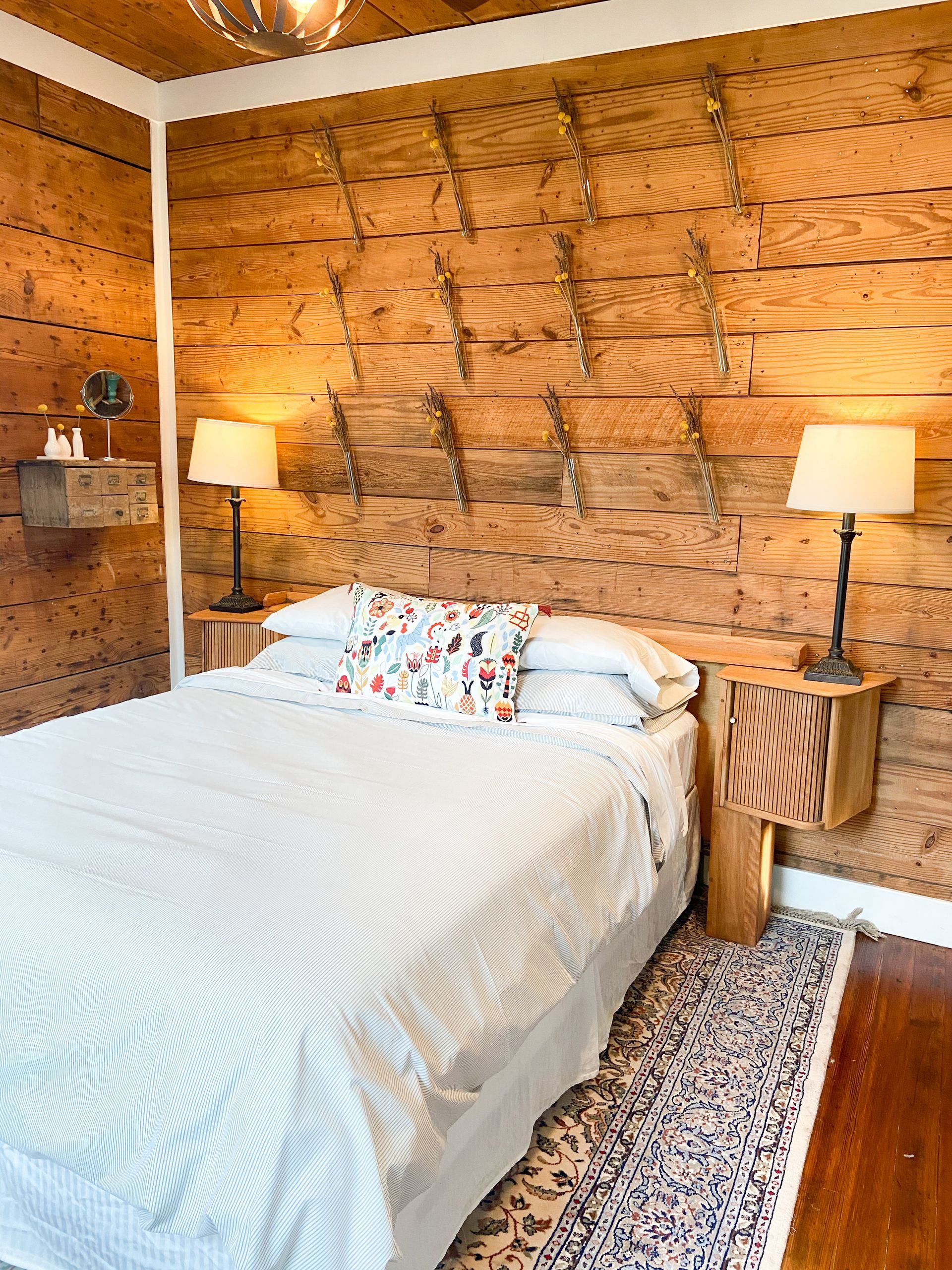 A bedroom with a bed , nightstands , lamps and a wooden wall.