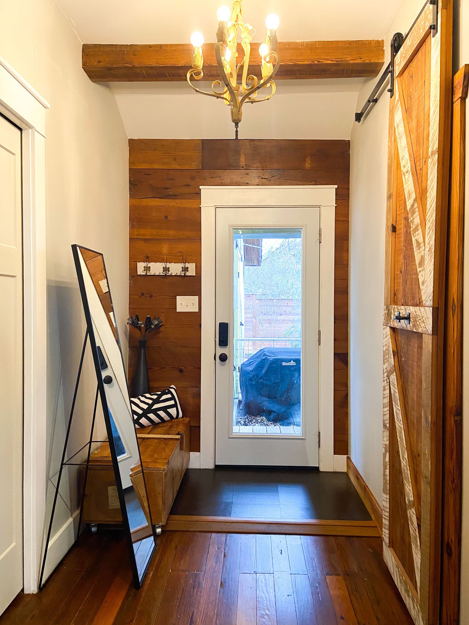 A hallway with wooden walls , hardwood floors , a mirror and a chandelier.