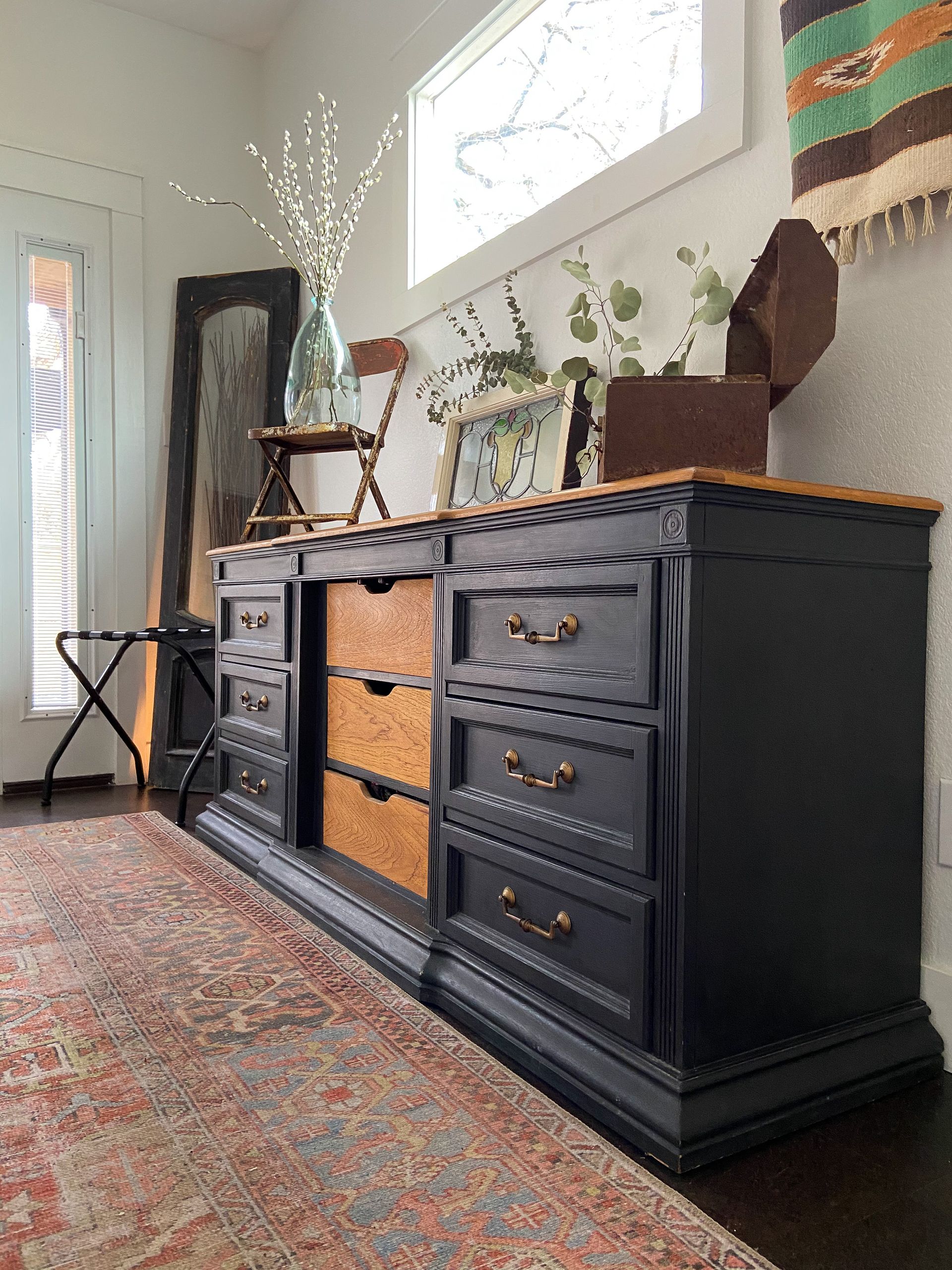 A black dresser is sitting in a living room next to a window.