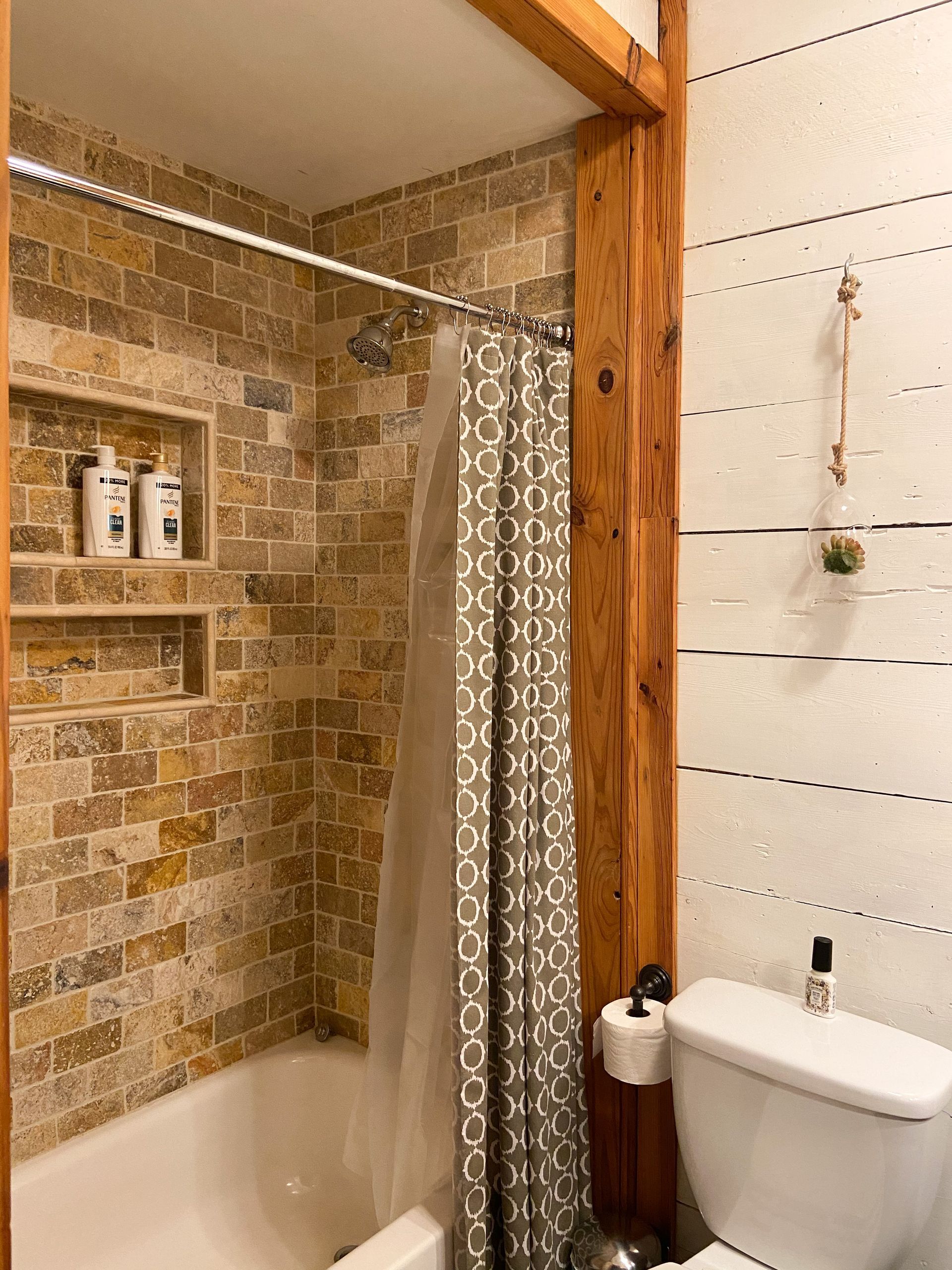A bathroom with a bathtub , toilet , shower and brick wall.