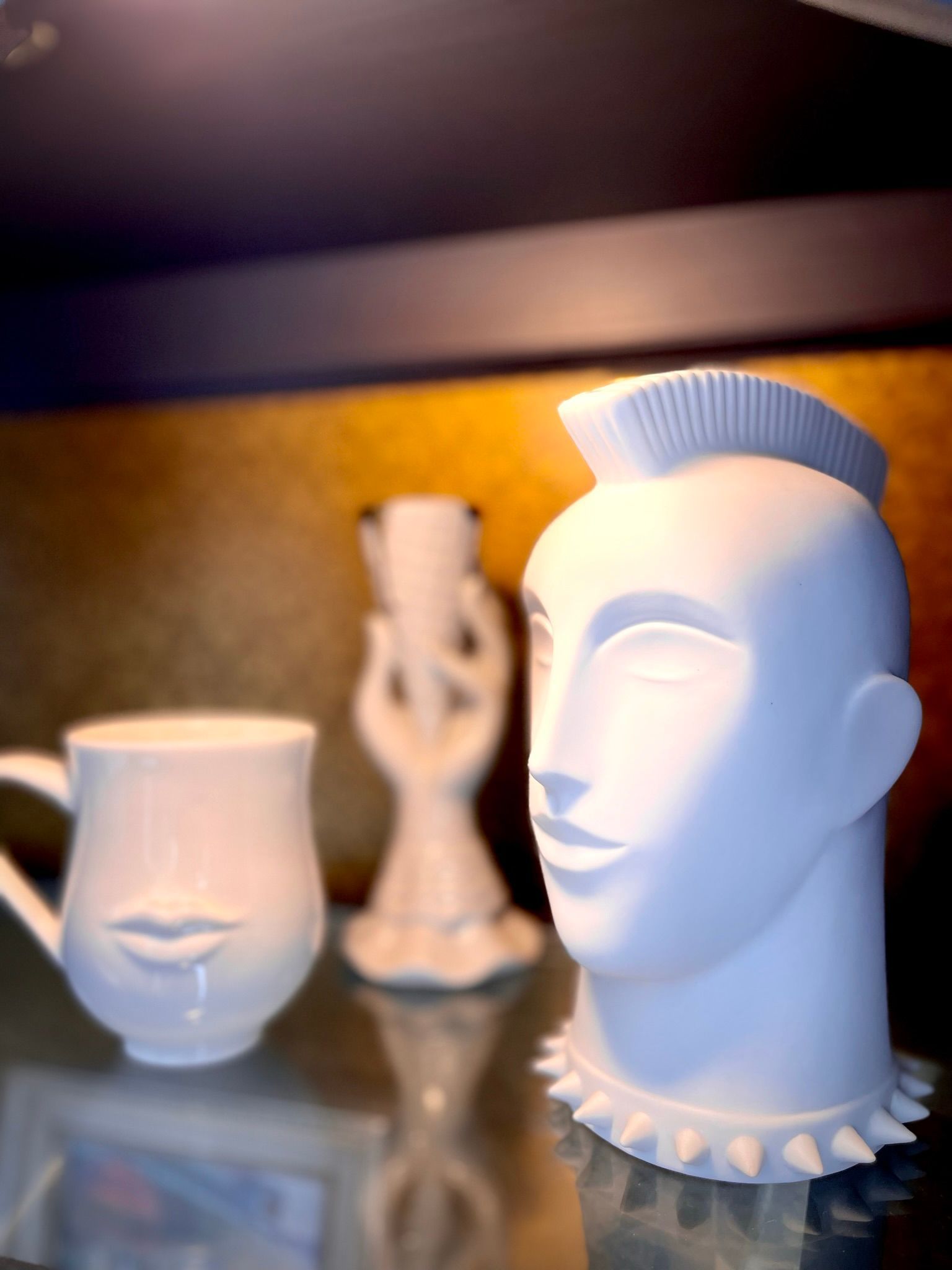 A white vase with spikes on it sits on a glass table