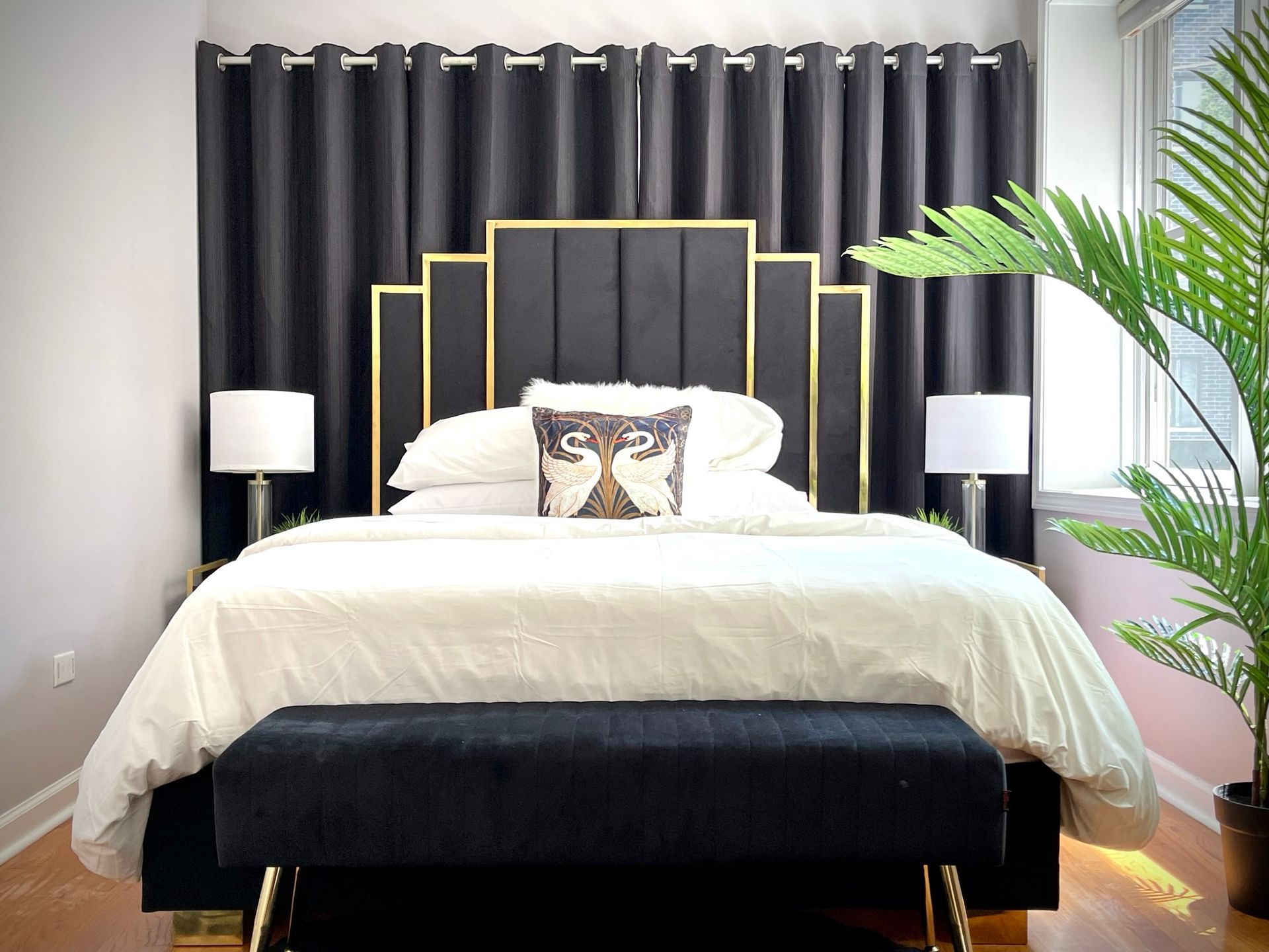 A bedroom with a bed , lamps , a bench and a plant.