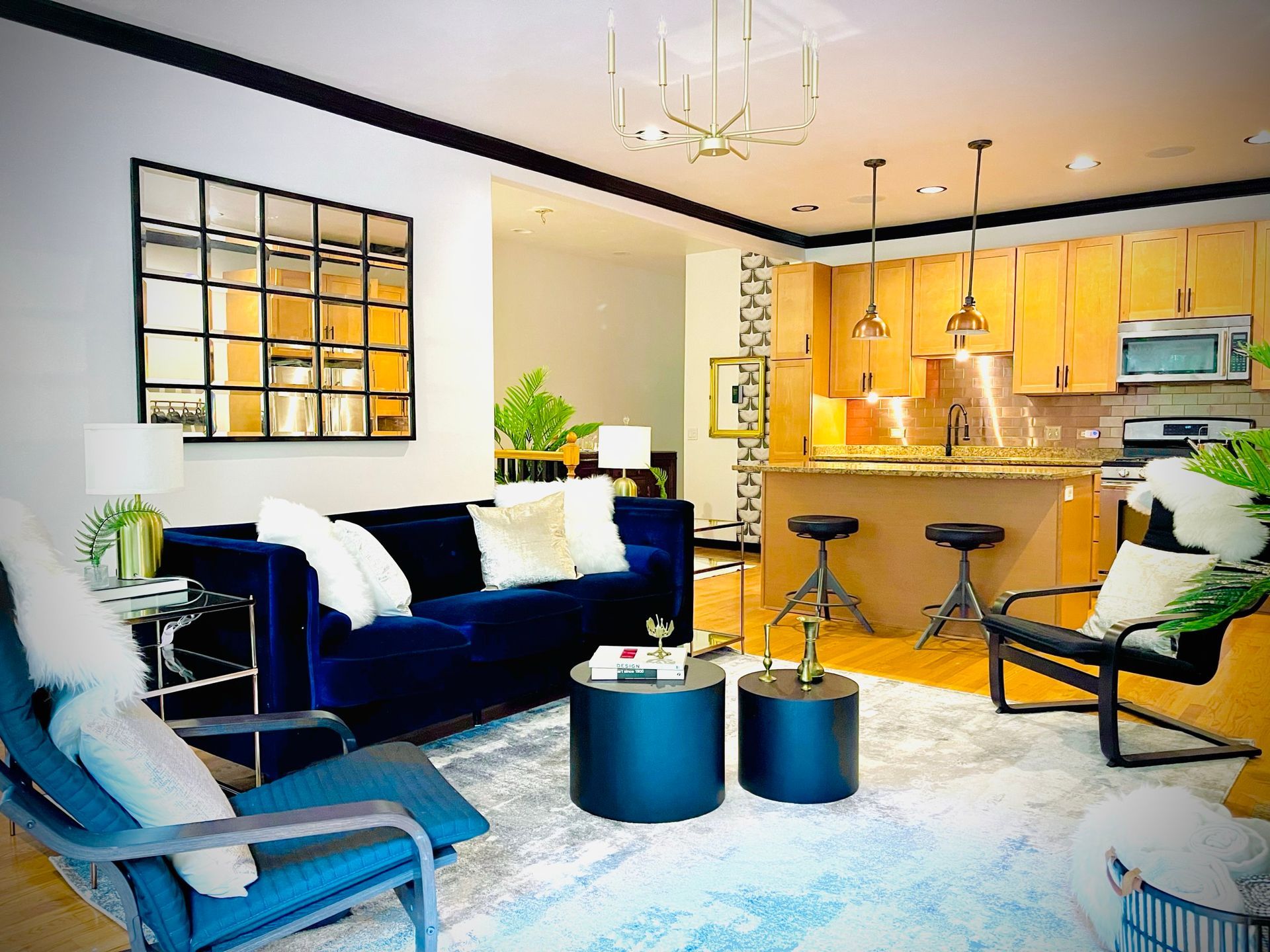 A living room with a blue couch , chairs , tables and a mirror on the wall.