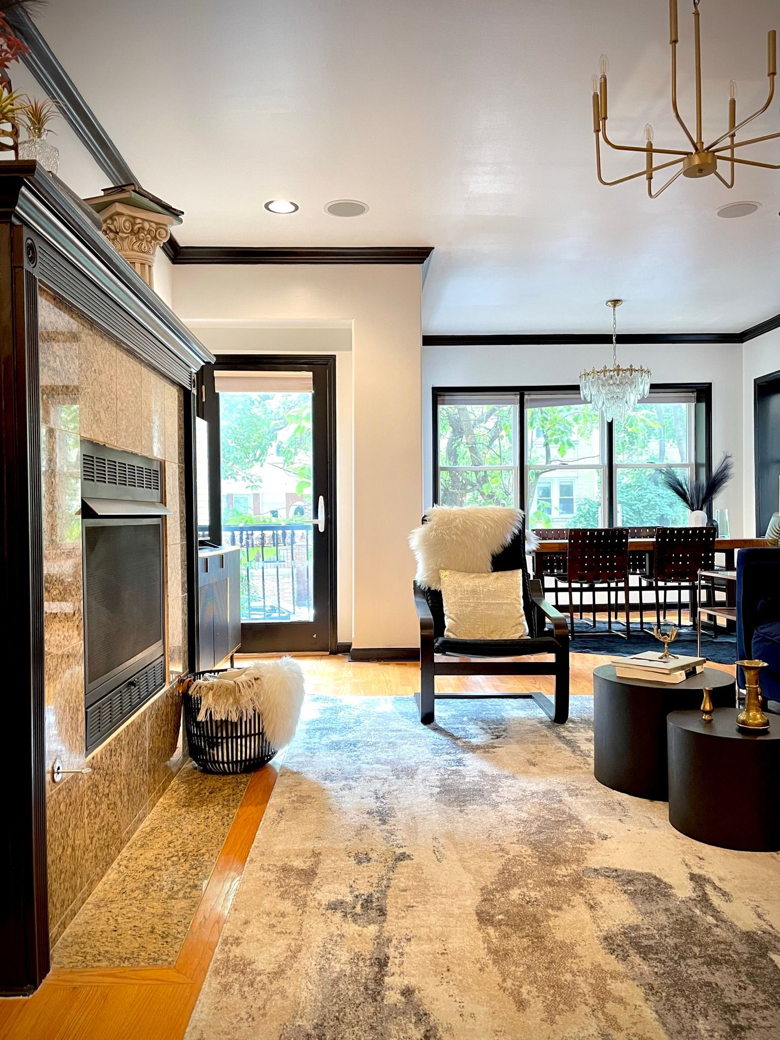A living room with a fireplace , chairs , tables and a chandelier.