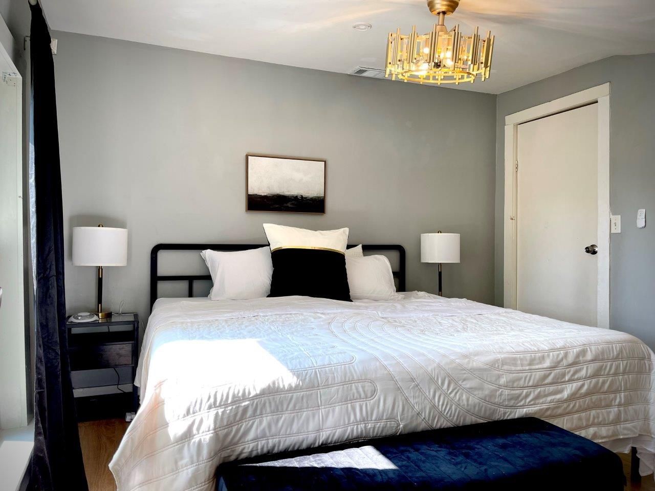 A bedroom with a bed , lamps , nightstands and a chandelier.