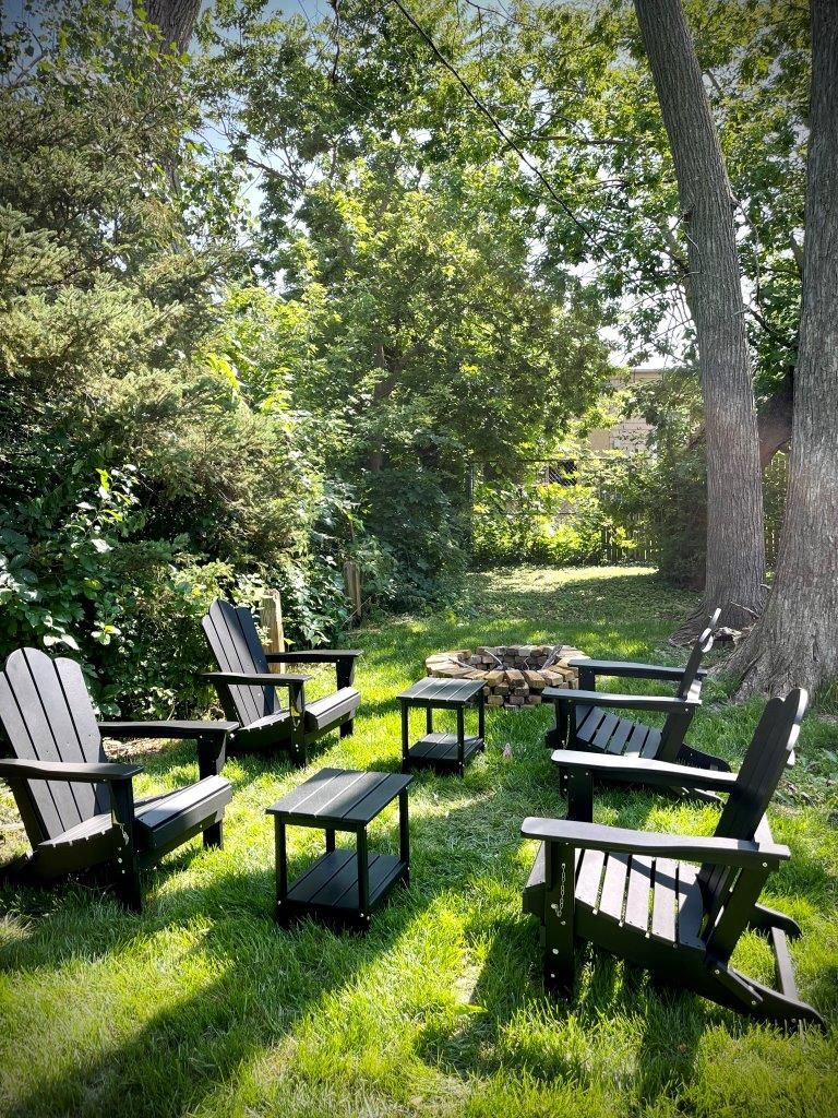 A group of chairs and tables are sitting in the grass next to a fire pit.