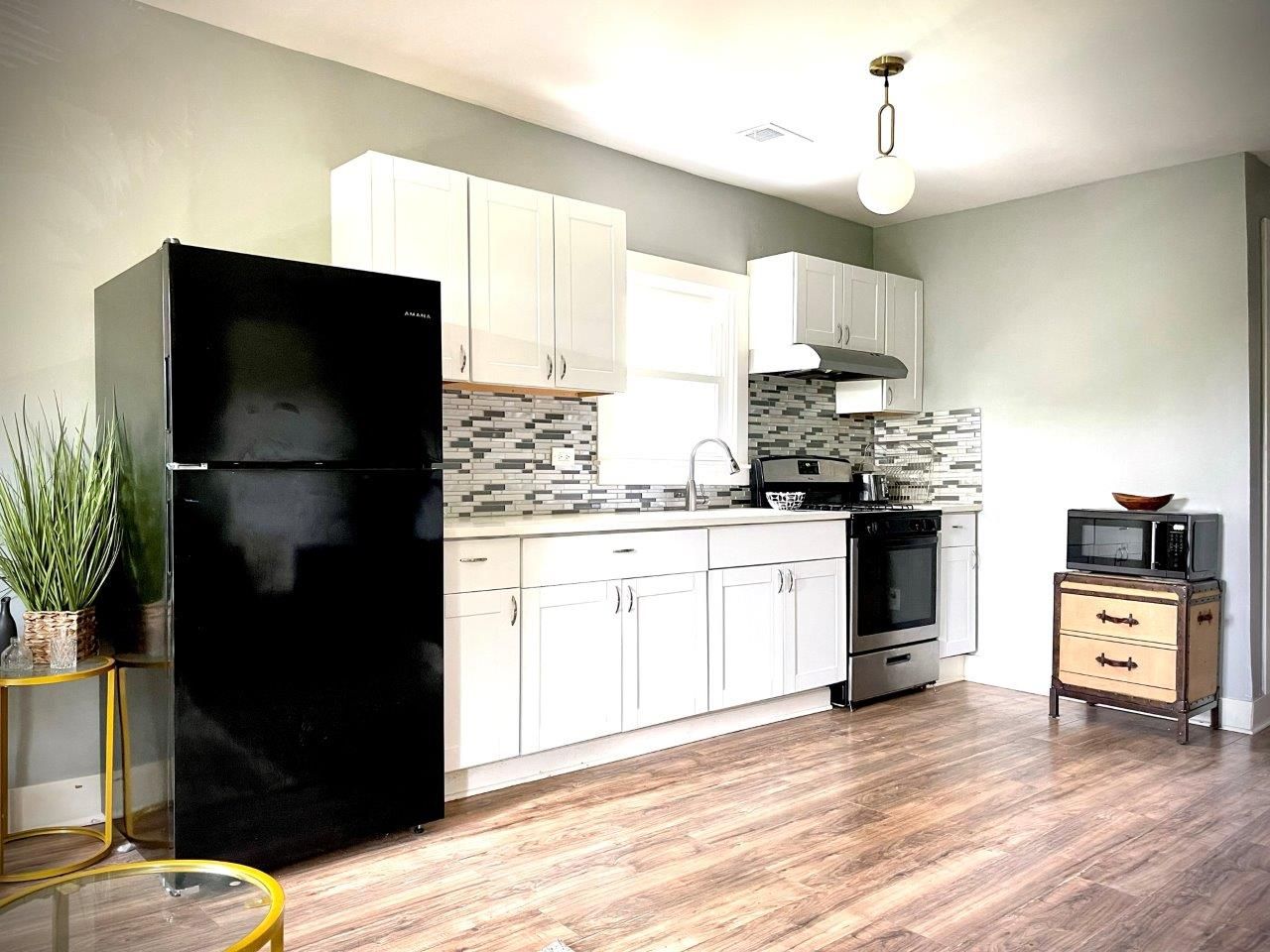 A kitchen with white cabinets , a black refrigerator , a stove , and a microwave.