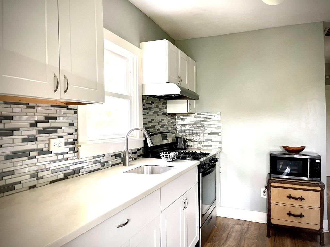 A kitchen with white cabinets , a sink , a stove and a microwave.