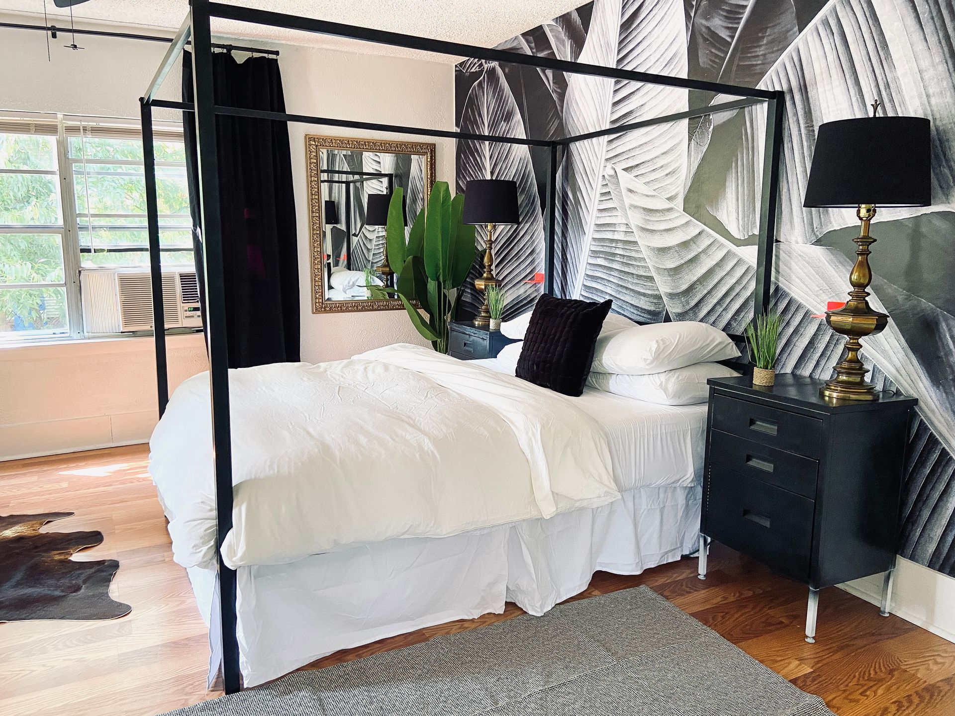A bedroom with a canopy bed , nightstand , mirror and lamp.