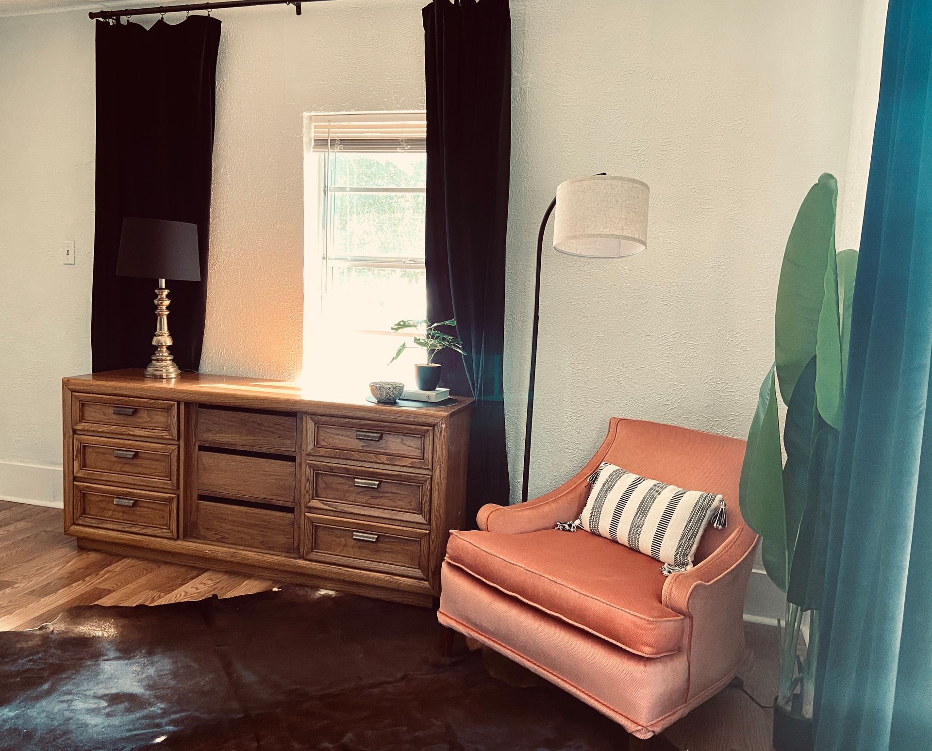 A living room with a chair , dresser , lamp and window.