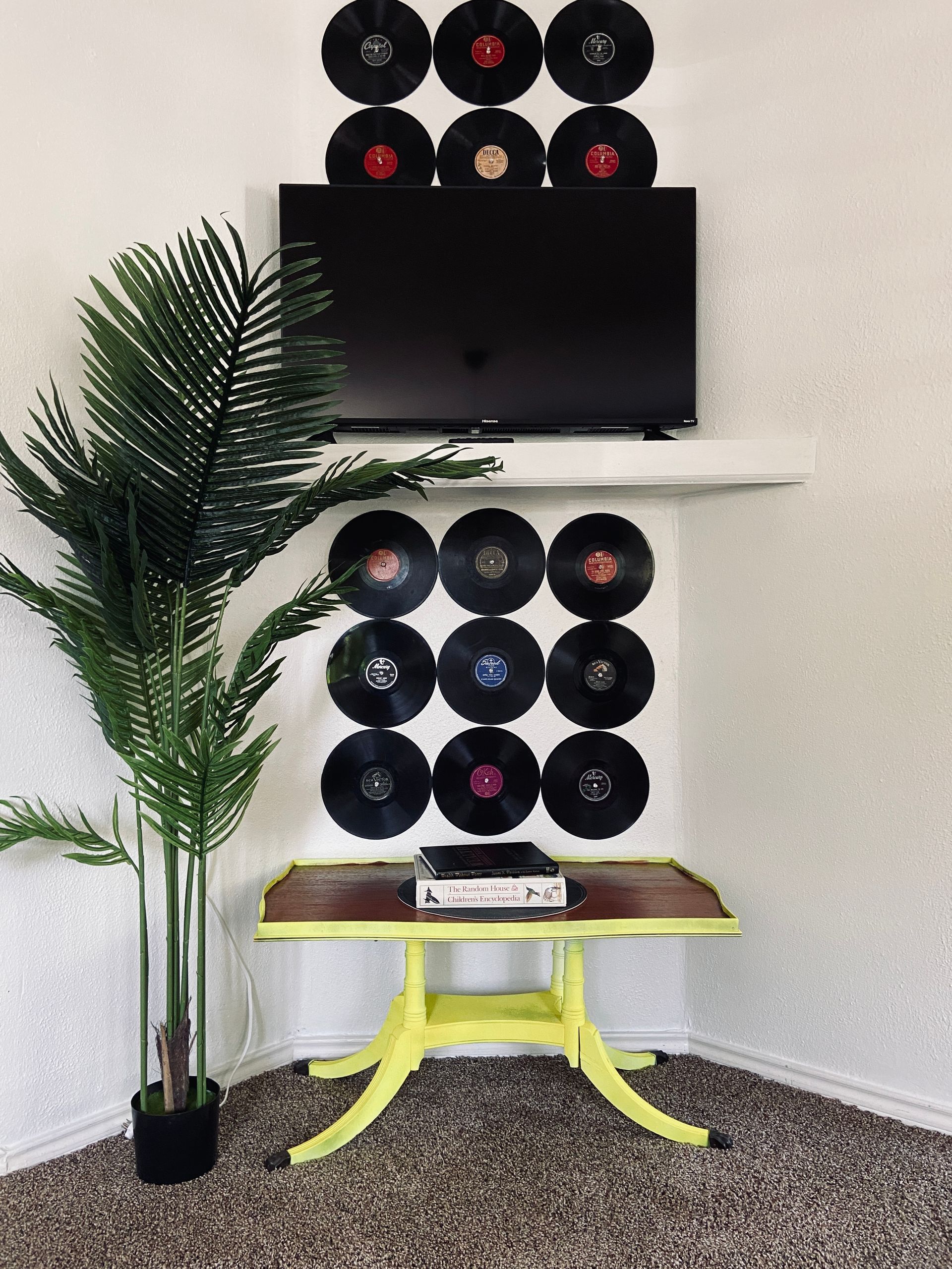 A living room with a yellow table , a plant , and a television.