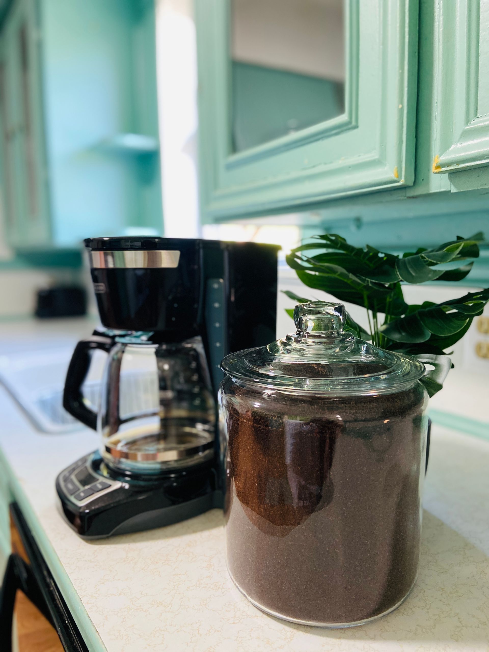 A coffee maker and a jar of coffee beans are on a kitchen counter.