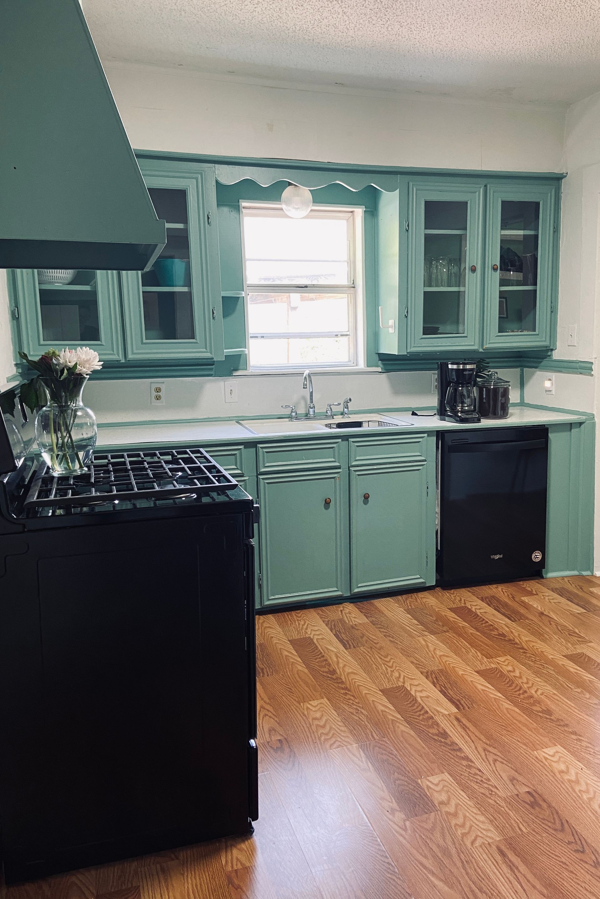 A kitchen with green cabinets and a black stove