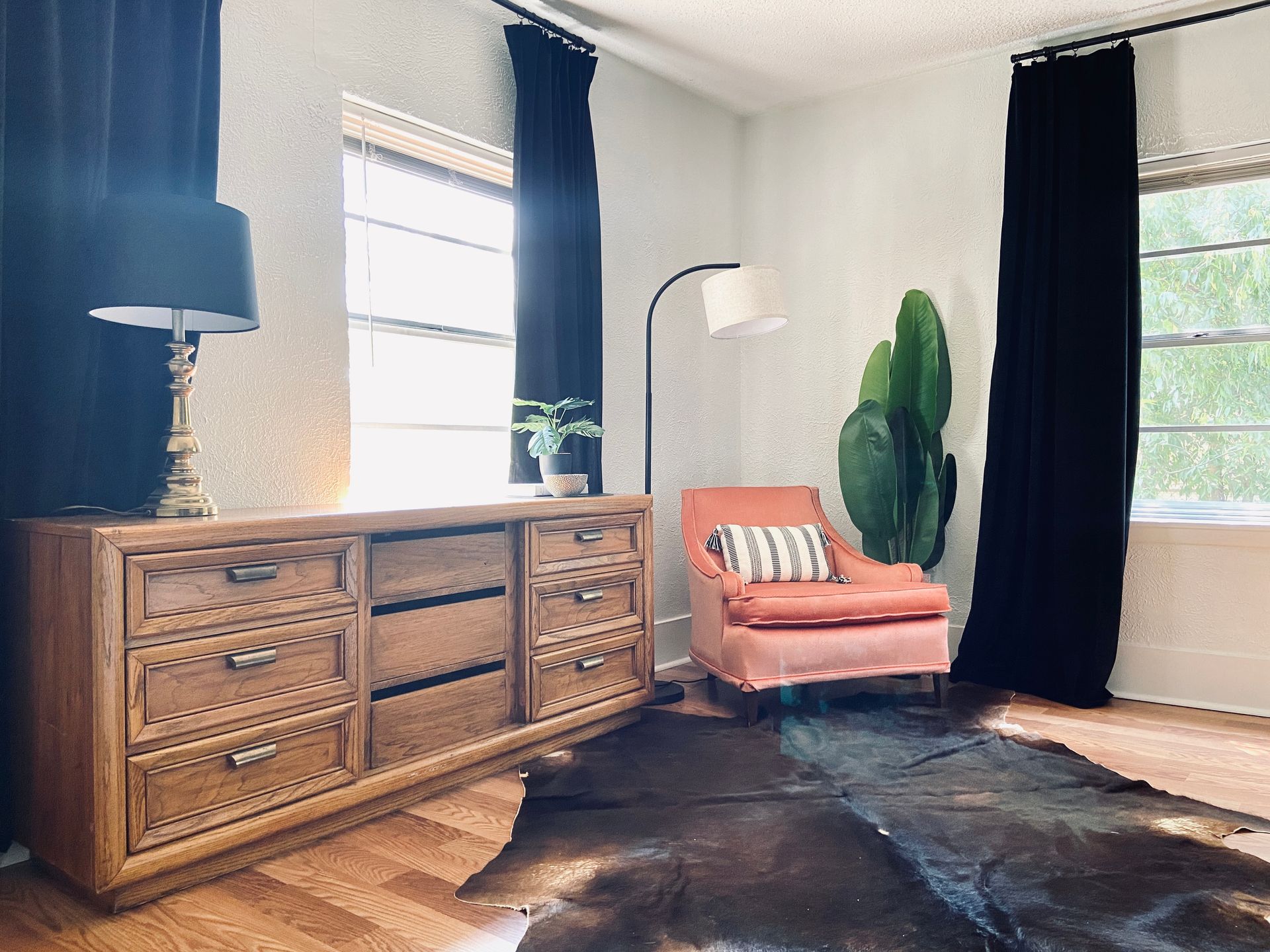 A living room with a dresser , chair , rug , lamp and window.