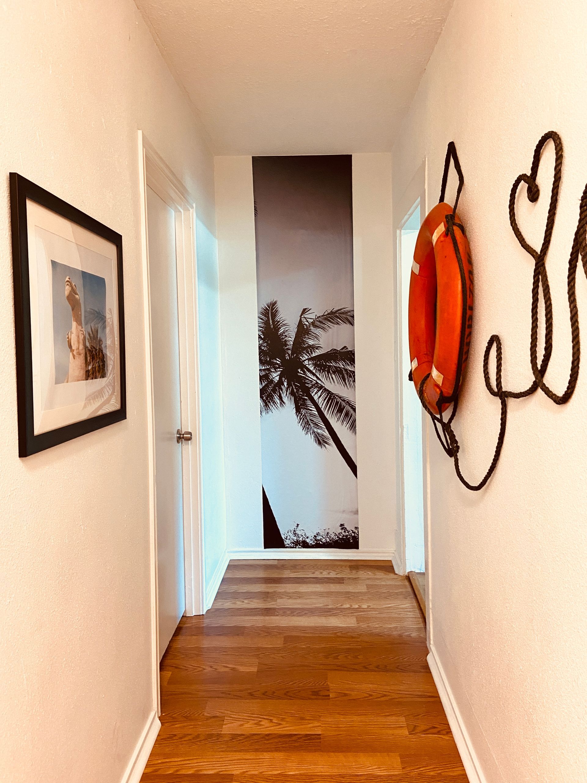 A hallway with a picture of a palm tree on the wall and a life preserver hanging on the wall.