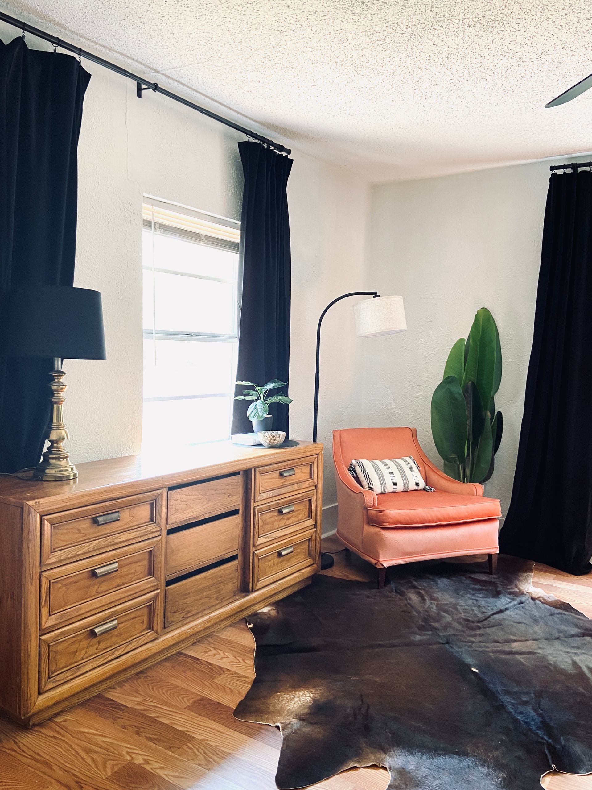 A living room with a dresser , chair , rug and lamp.