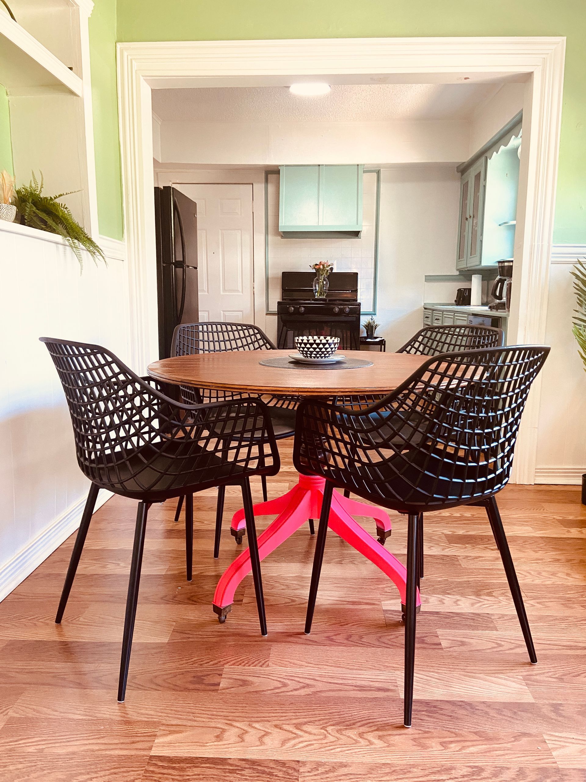 A dining room with a table and chairs and a kitchen in the background.