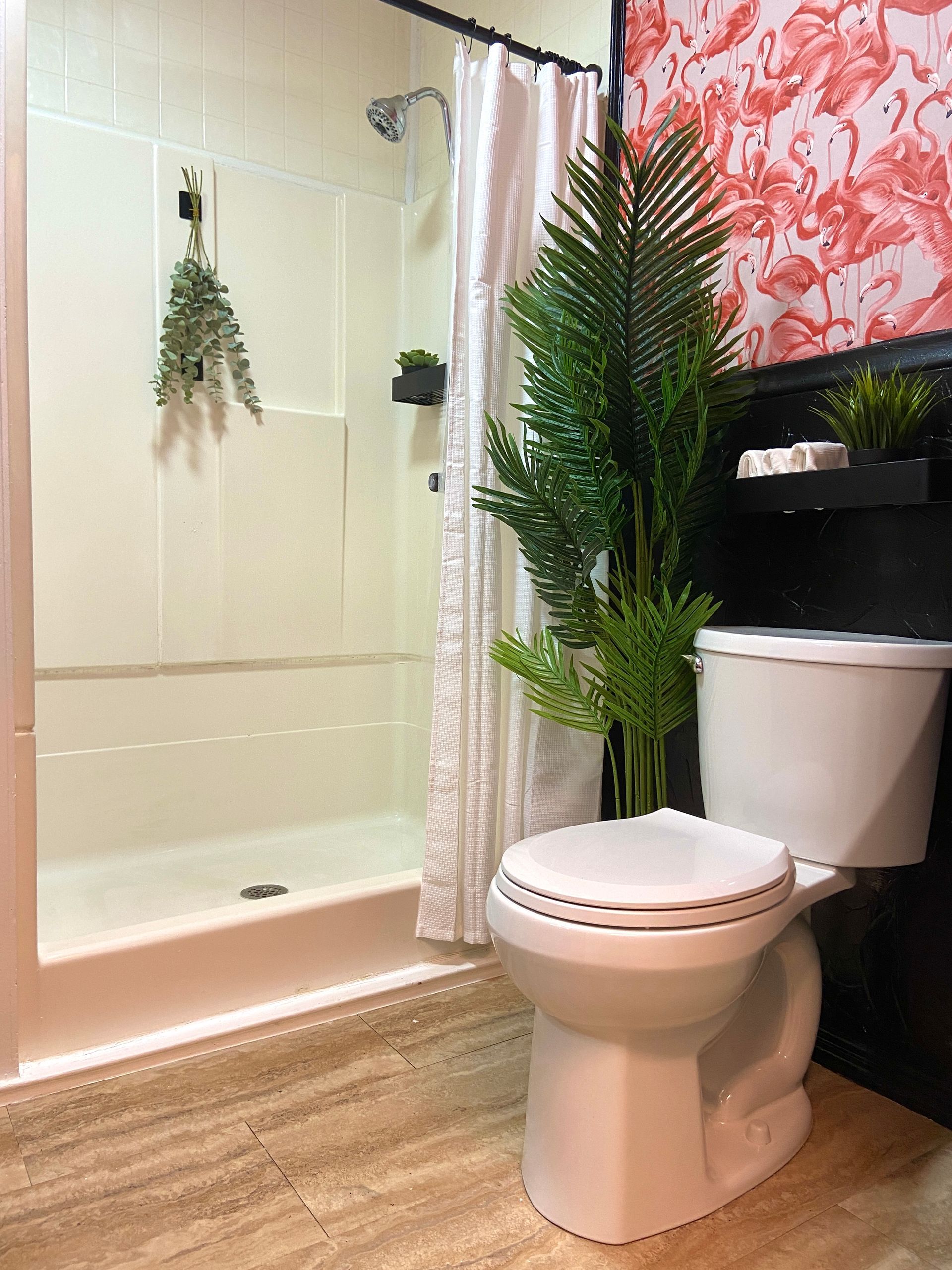 A bathroom with a toilet , shower , and plant.