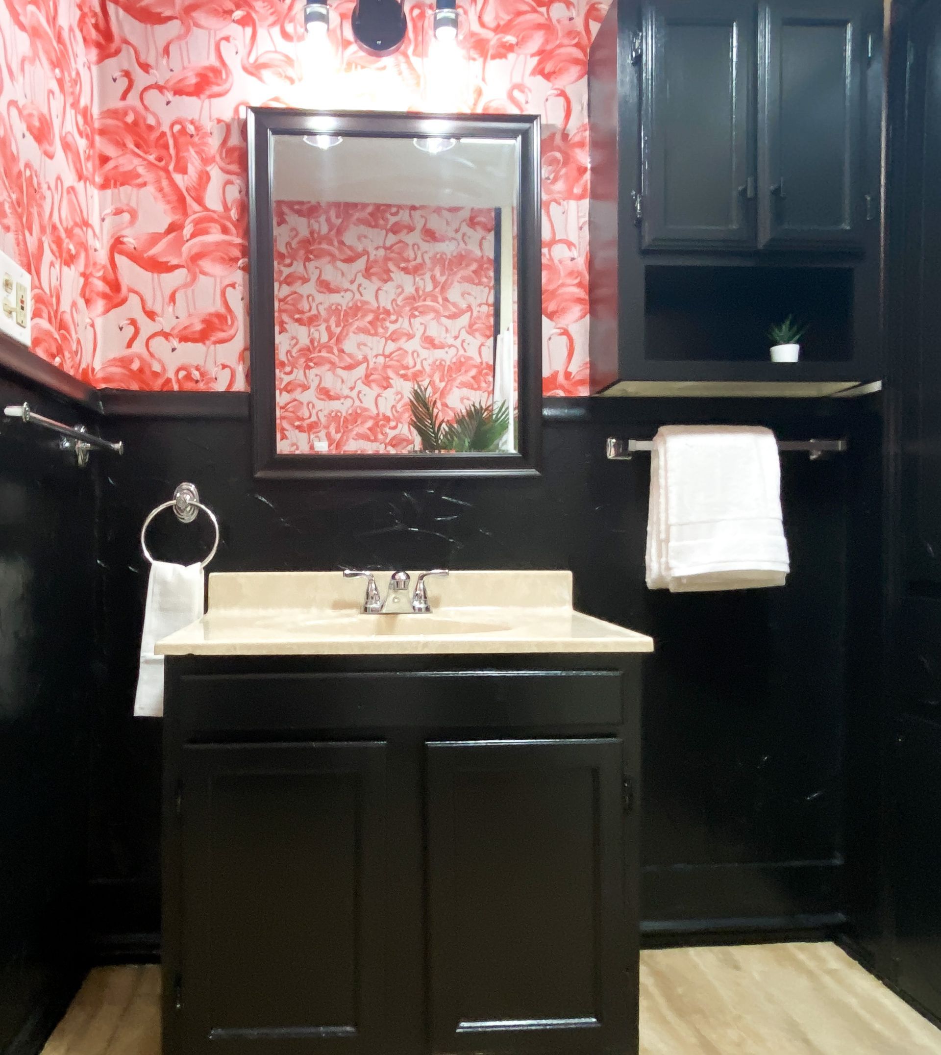A bathroom with flamingo wallpaper and black cabinets