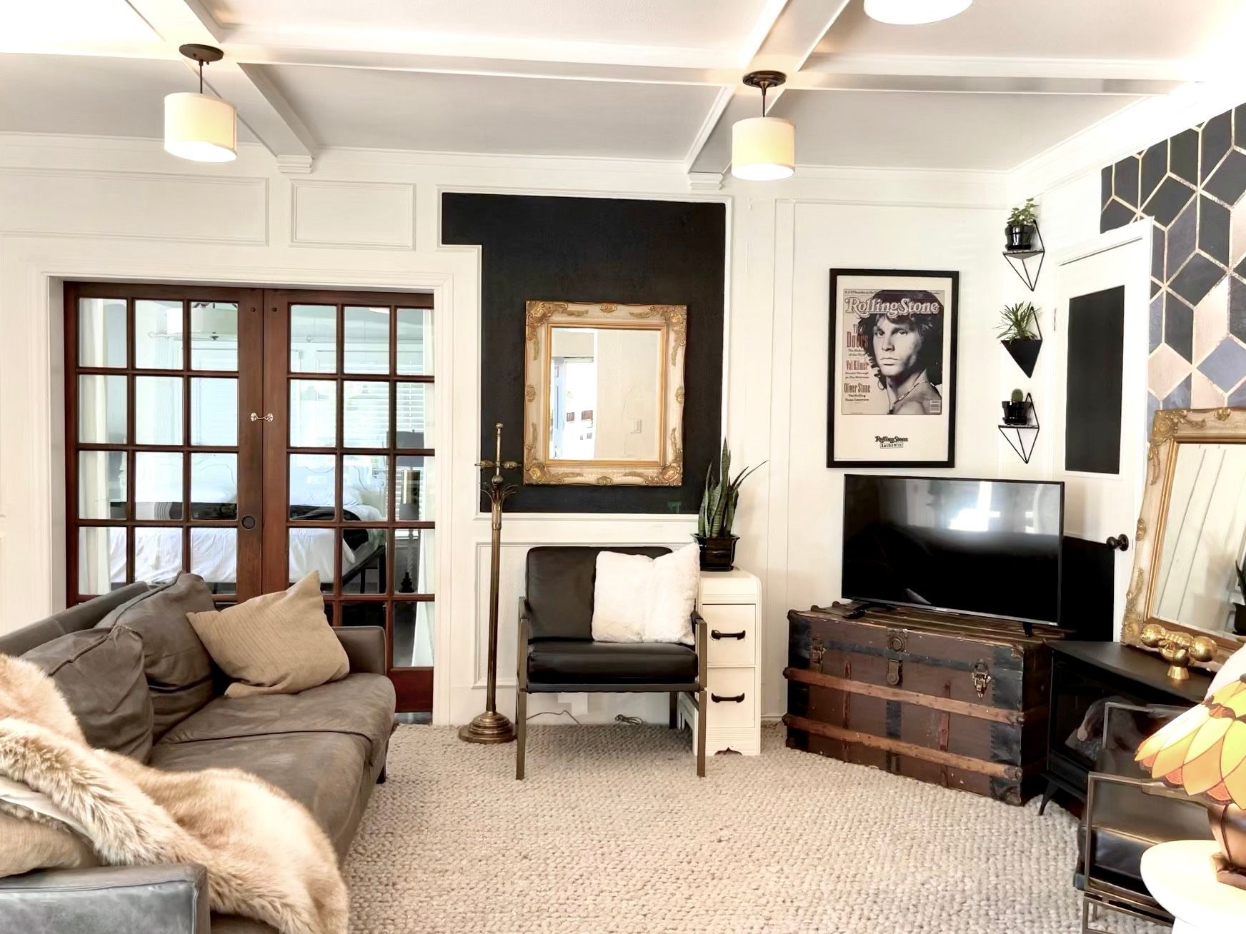 A living room with a couch , chair , television , trunk and mirror.