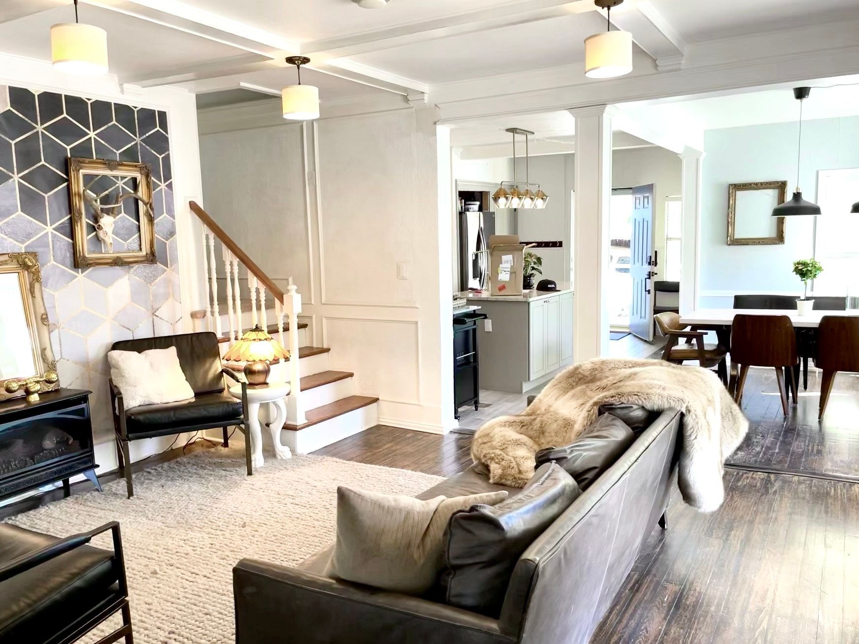 A living room with a couch , chairs , stairs and a dog laying on the couch.