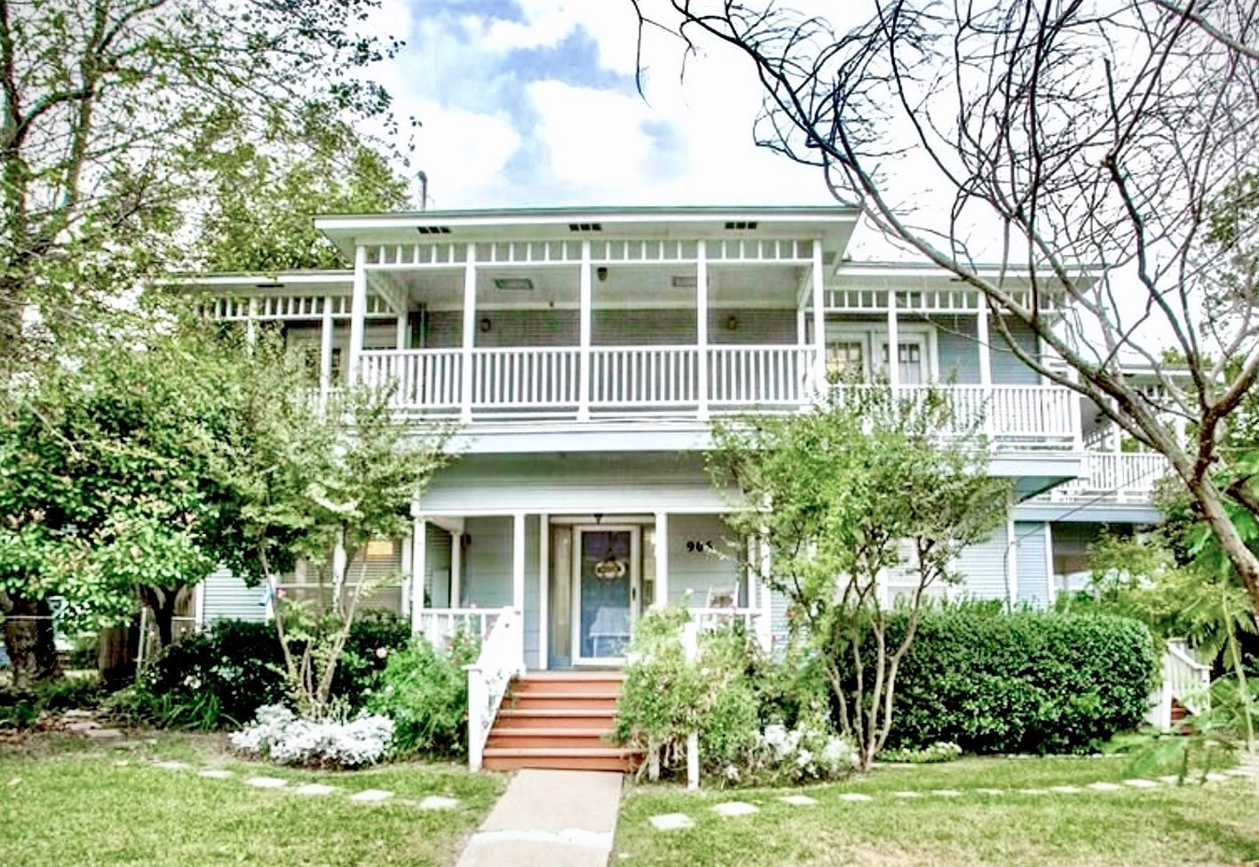 A large white house with a large porch and stairs surrounded by trees.