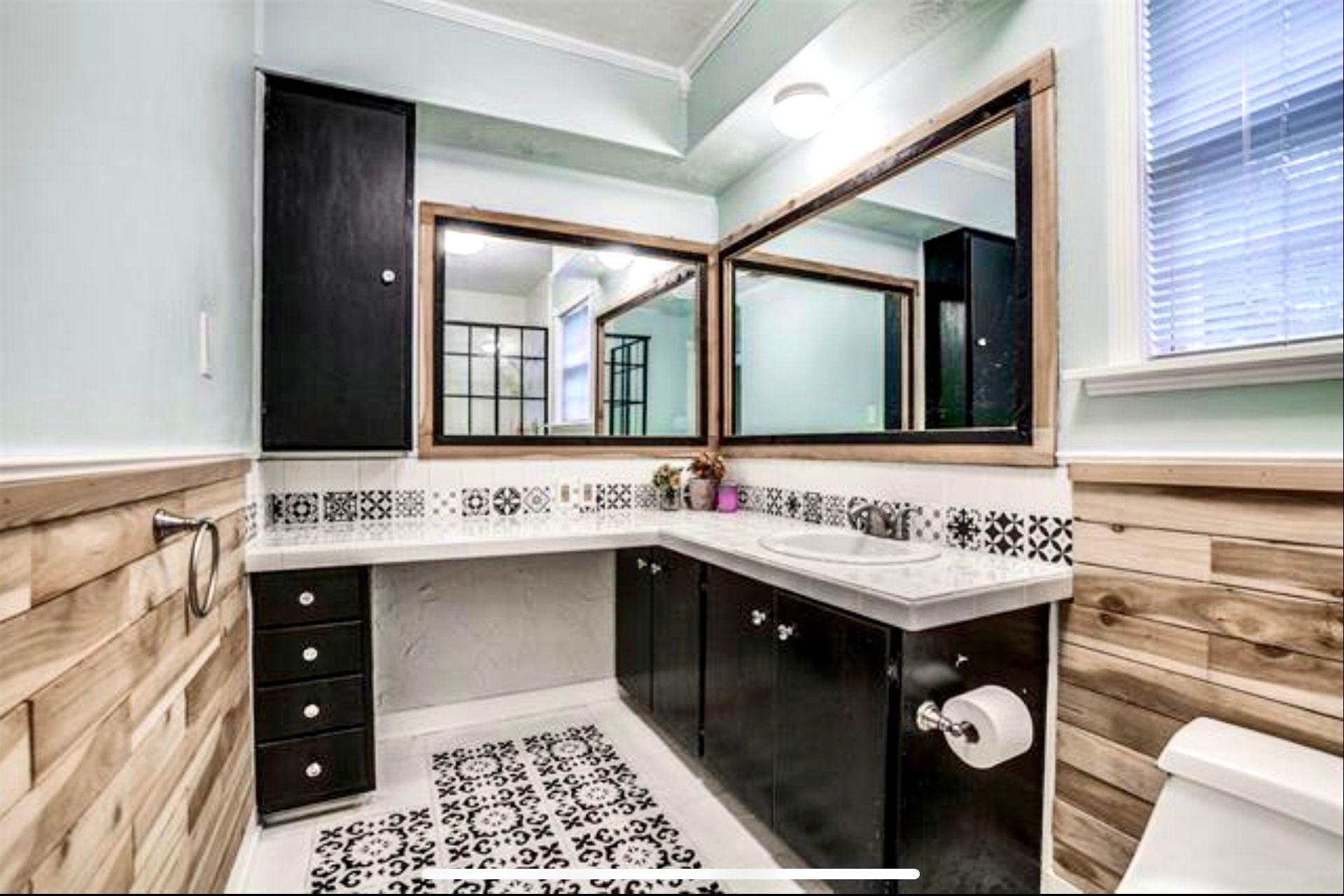 A bathroom with a toilet , sink , mirrors and wooden cabinets.
