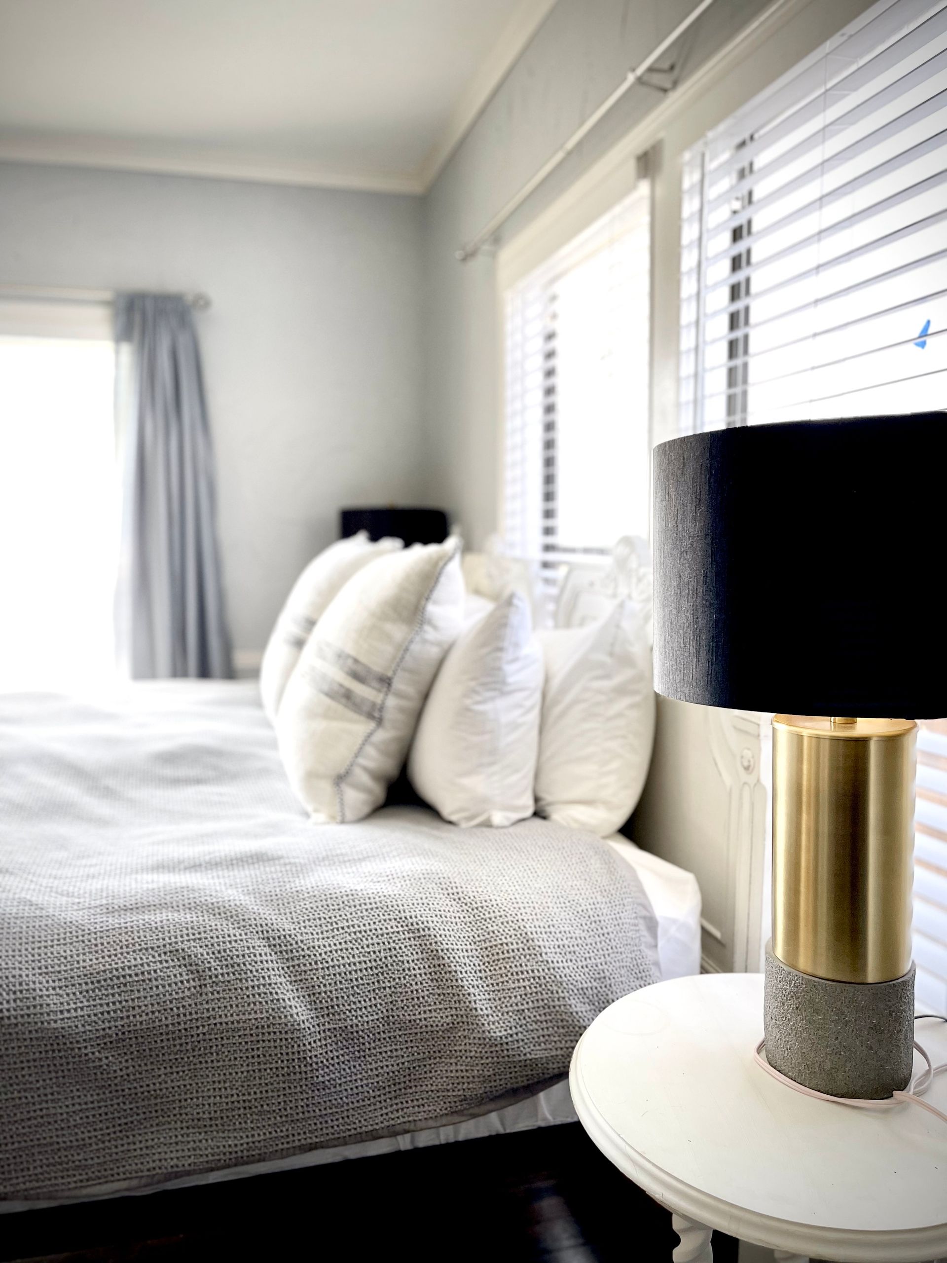 A bedroom with a bed , nightstand , lamp and window.